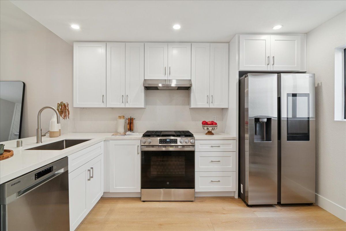 Bright modern kitchen with white cabinets, stainless steel appliances, and light wood flooring