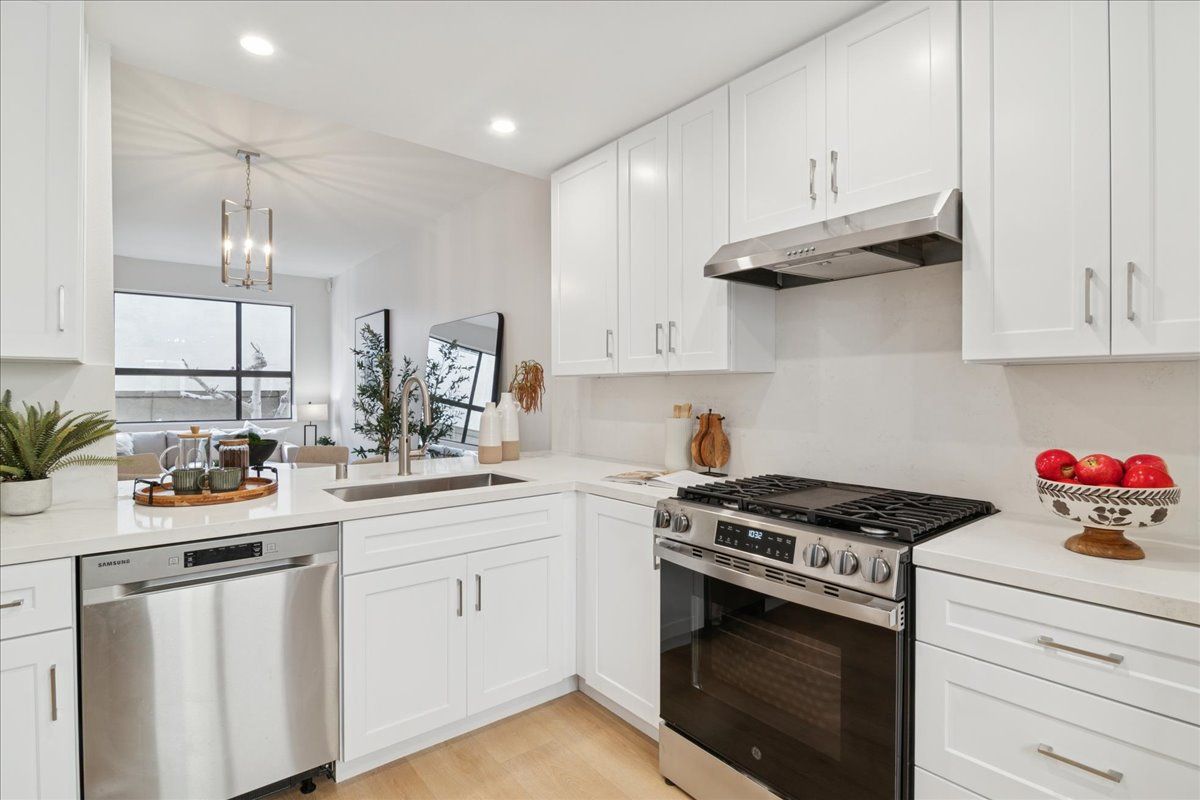 Bright white modern kitchen with stainless steel appliances, large window, and black stove.