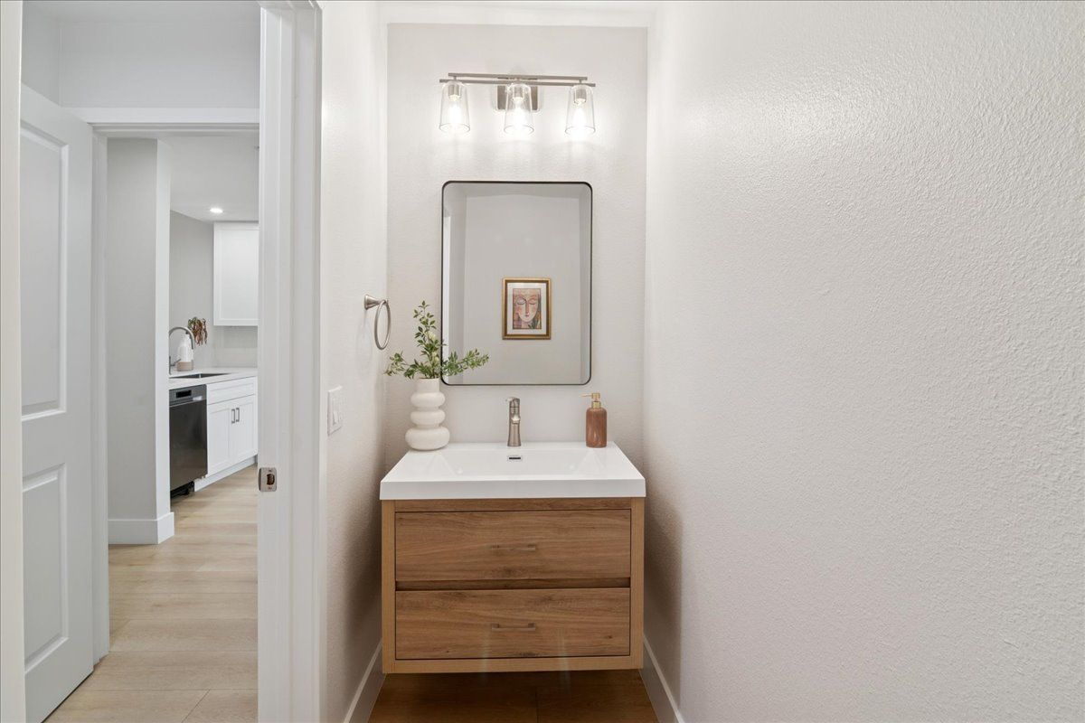 Bright hallway with a wooden vanity, mirror, and vase; open doorway leads to a kitchen.