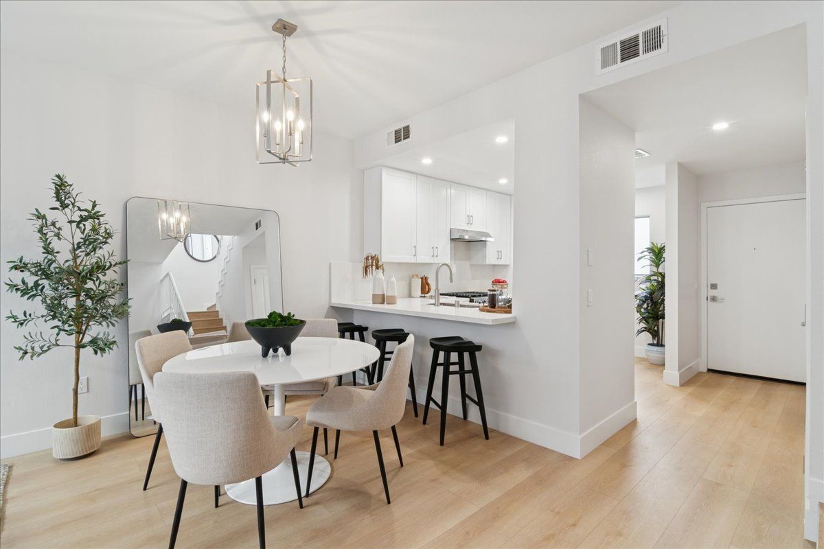 Bright open dining area with round table, beige chairs, chandelier, and white kitchen with black stools