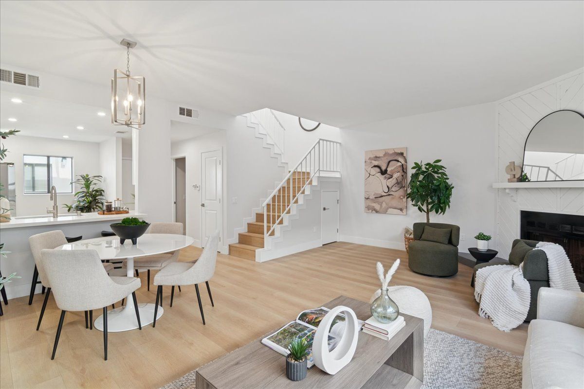 Bright modern open-plan living room and dining area with white decor, wood floors, and staircase