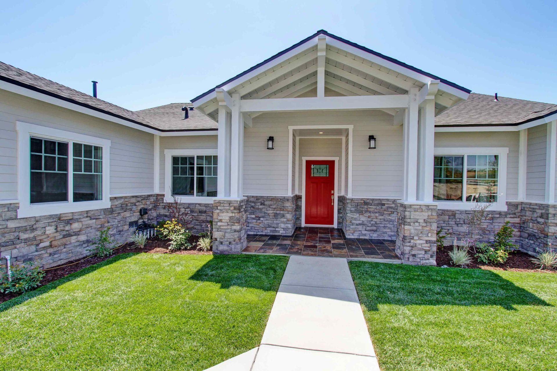 Single-story house with red front door, stone facade, and a green lawn with a walkway.