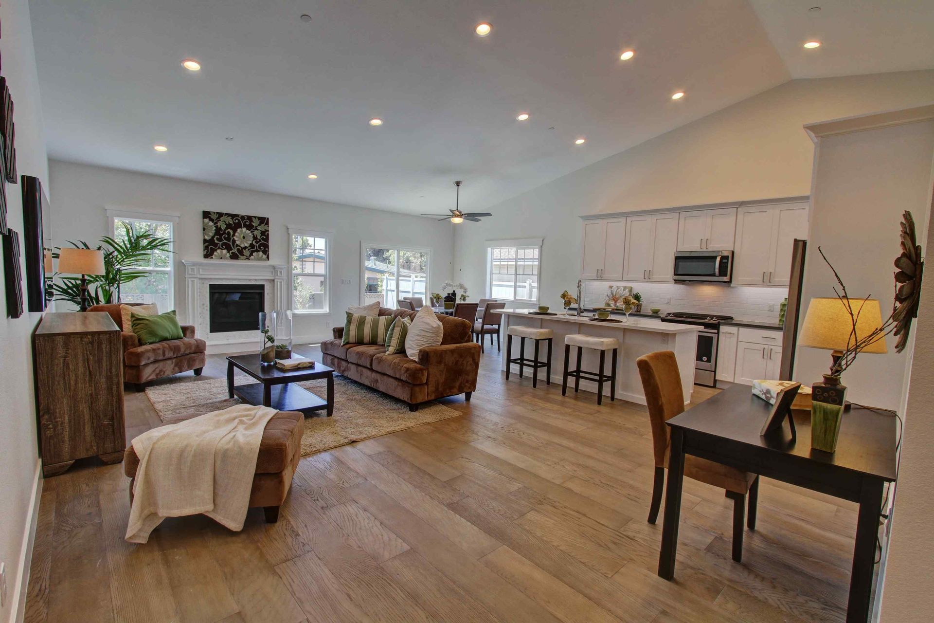 Bright open-plan living room with wood floors, sectional sofa, bar stools, and a fireplace