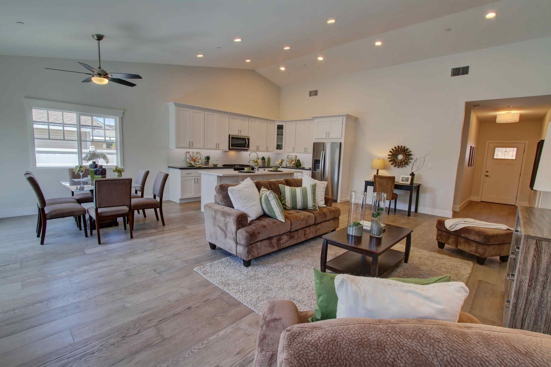 Bright open-plan living room and kitchen with beige furniture, dining table, and ceiling fan