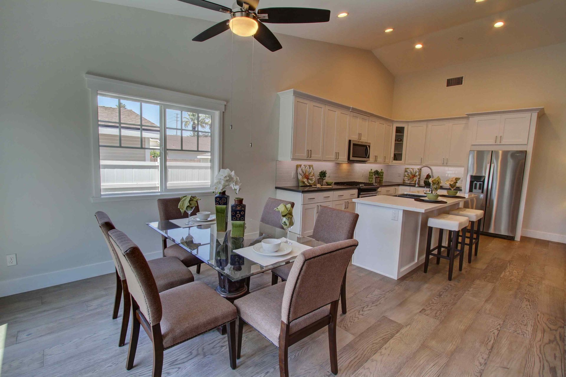 Bright open dining and kitchen area with a table, chairs, white island, and ceiling fan in a modern home