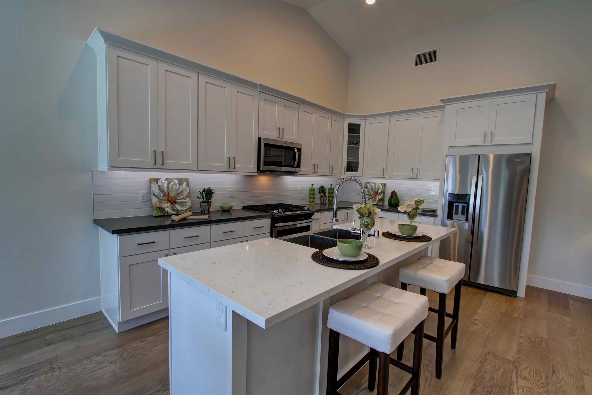Modern white kitchen with island, stools, stainless steel appliances, and wood flooring