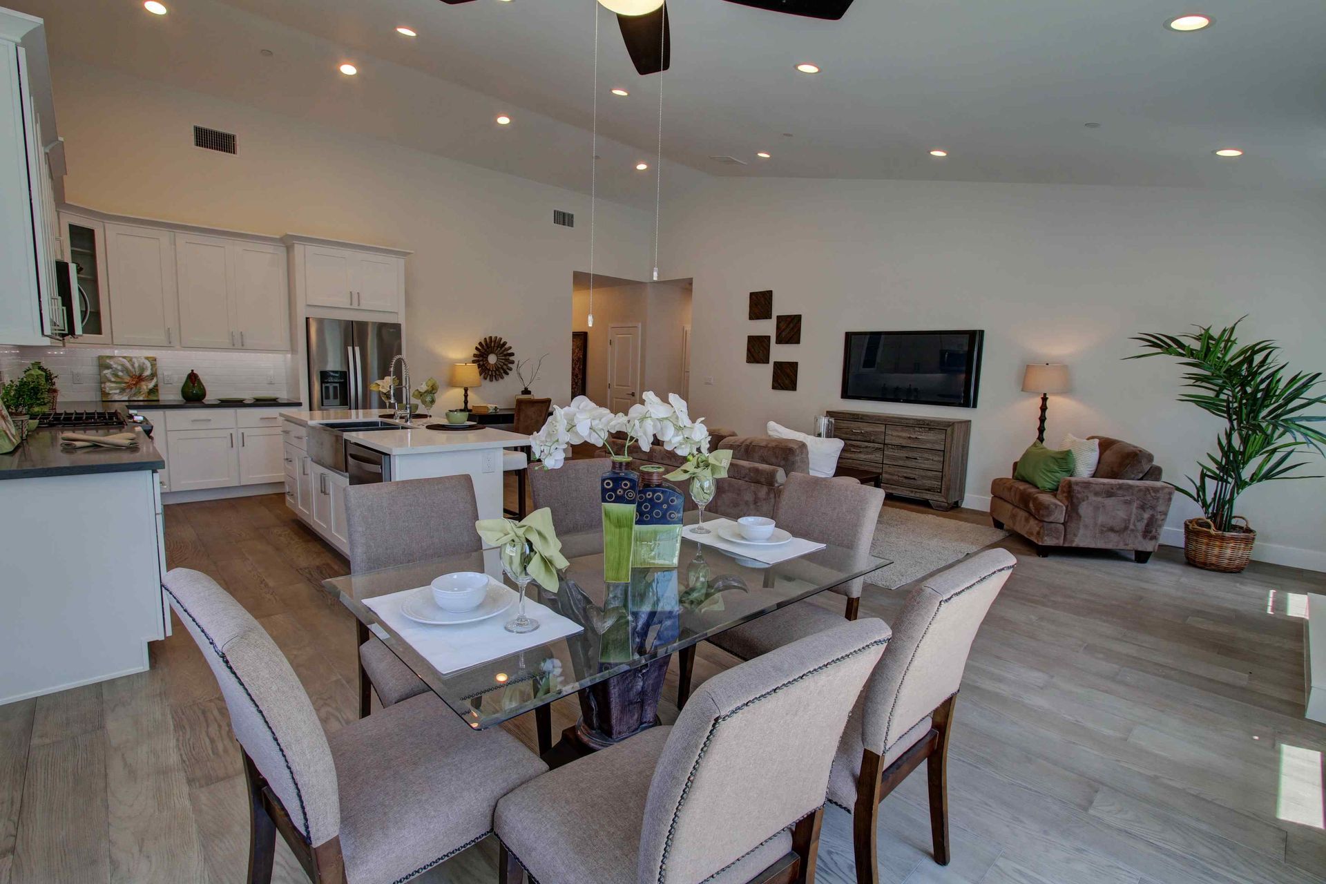 Bright open-concept living room and dining area with gray furniture, TV, fireplace, and kitchen in background