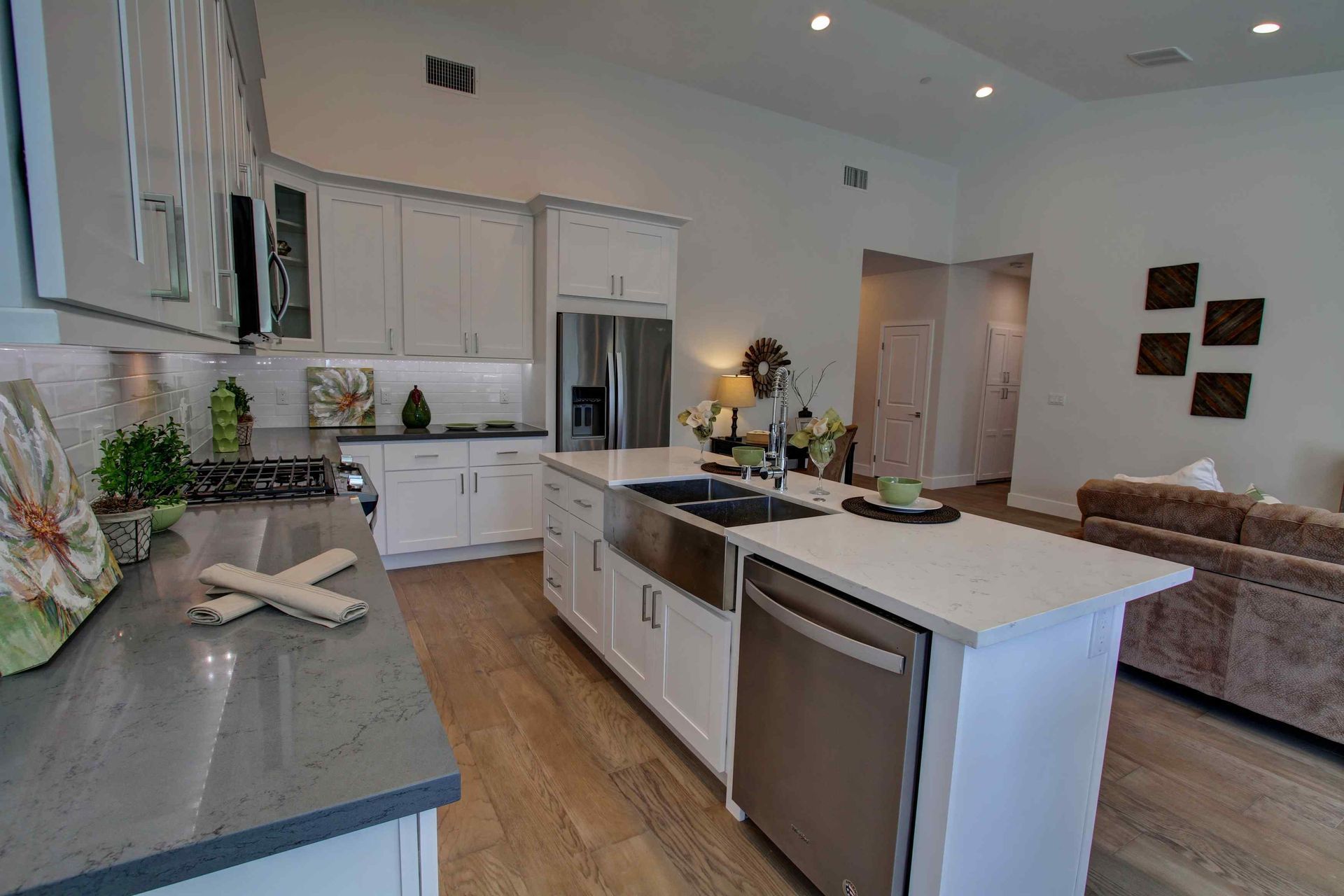 Bright modern kitchen with white cabinets, wood floors, island, and beige sofa in the background
