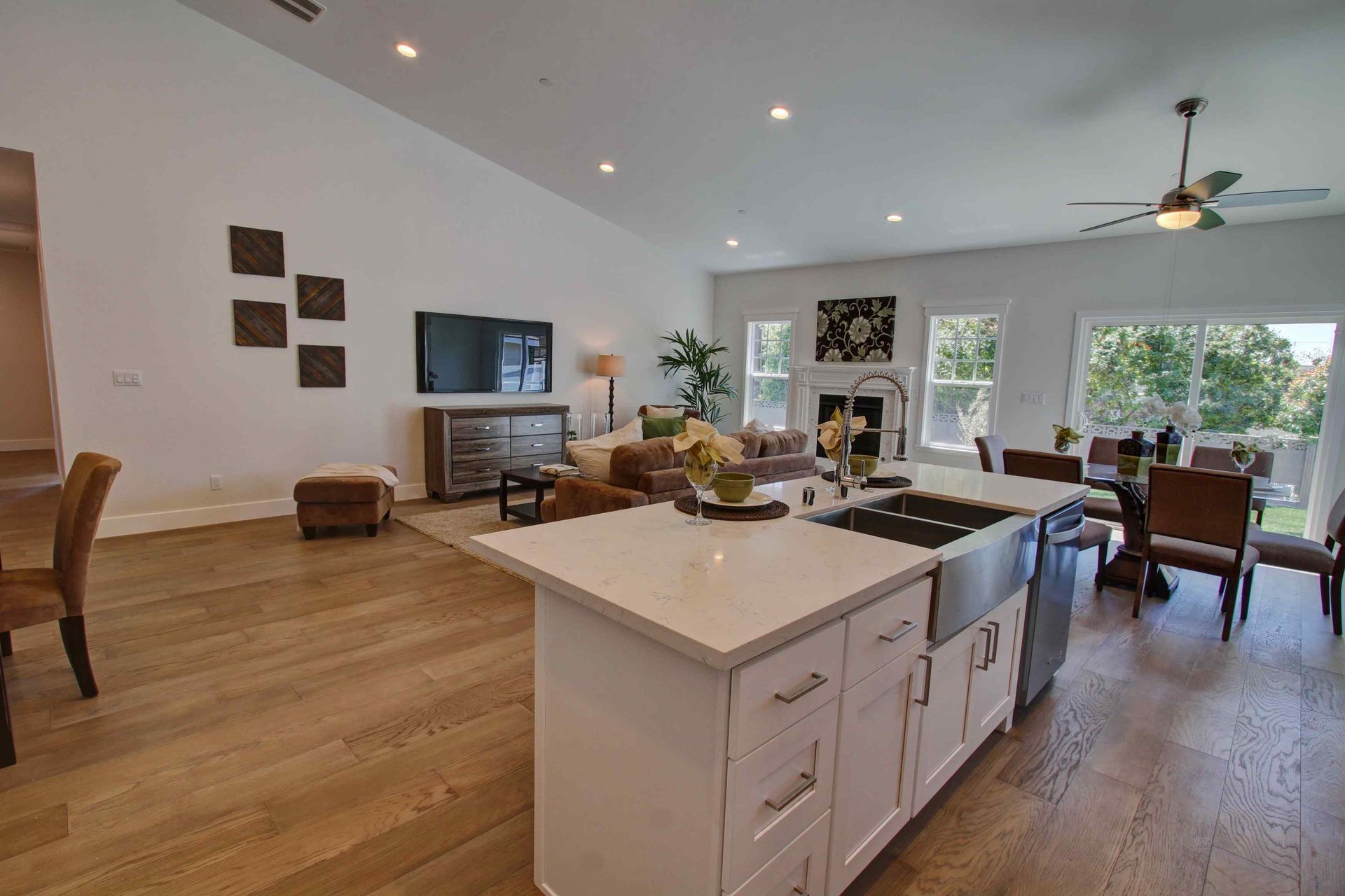 Bright modern kitchen and living area with island, wood floors, and large windows overlooking a patio.