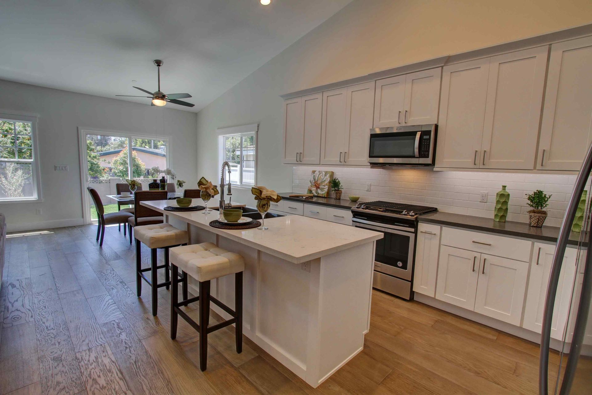 Bright modern kitchen with island and stools opening to a dining area and large windows