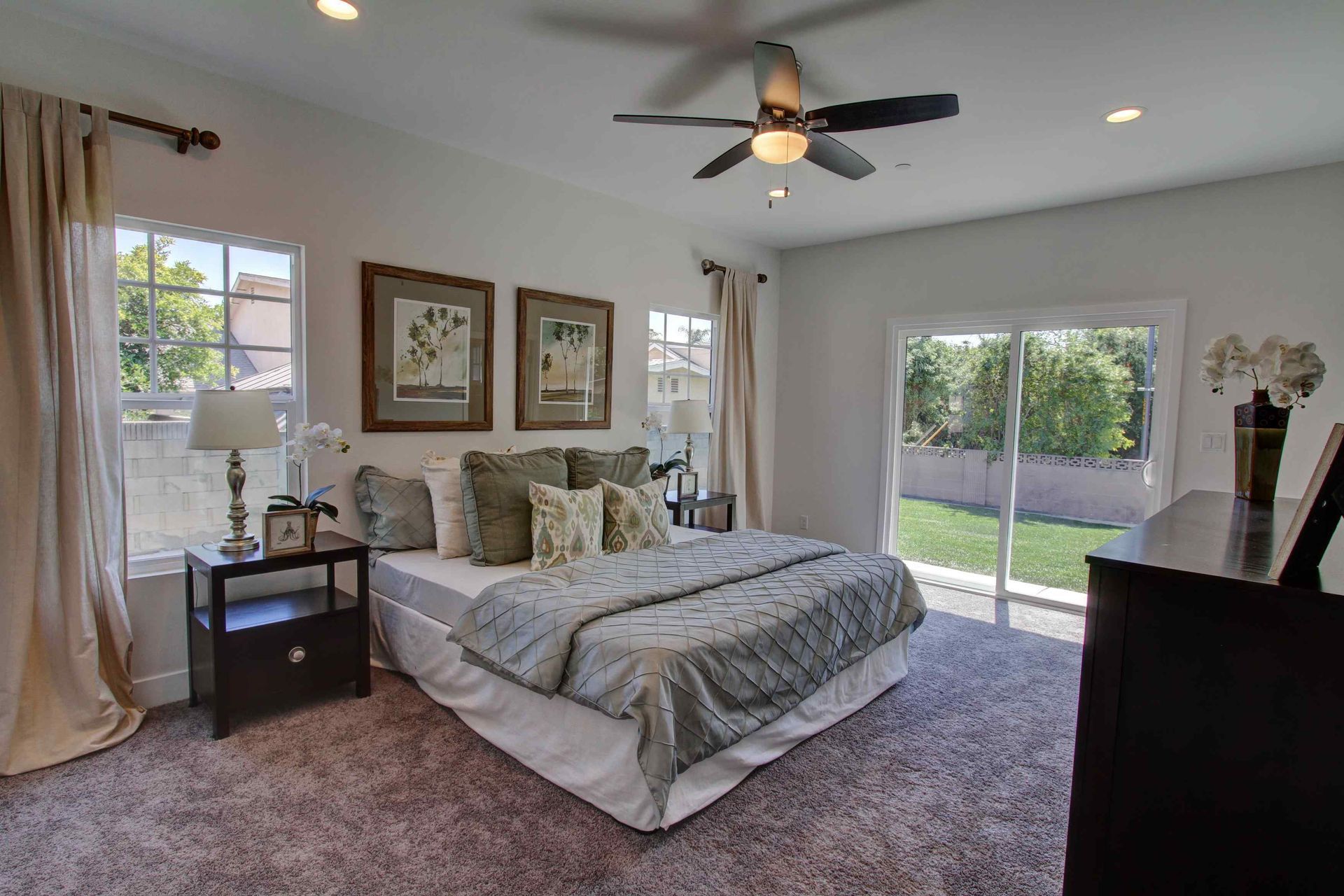 Bright bedroom with a large bed, ceiling fan, nightstand, and sliding glass doors to a green patio.