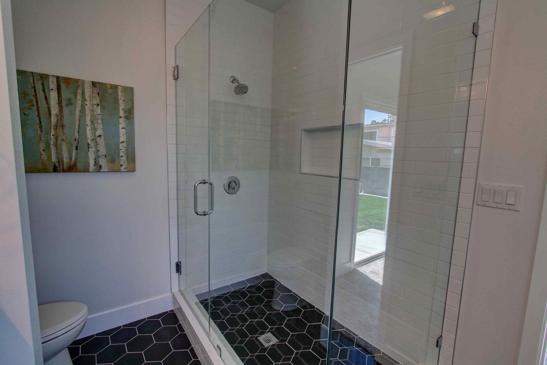 Modern bathroom with glass shower, black hex tile floor, and white walls