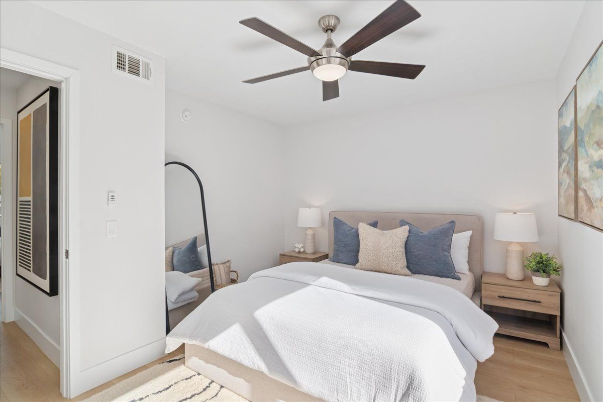Bright bedroom with a bed, ceiling fan, nightstand, mirror, and wall art in a minimalist room