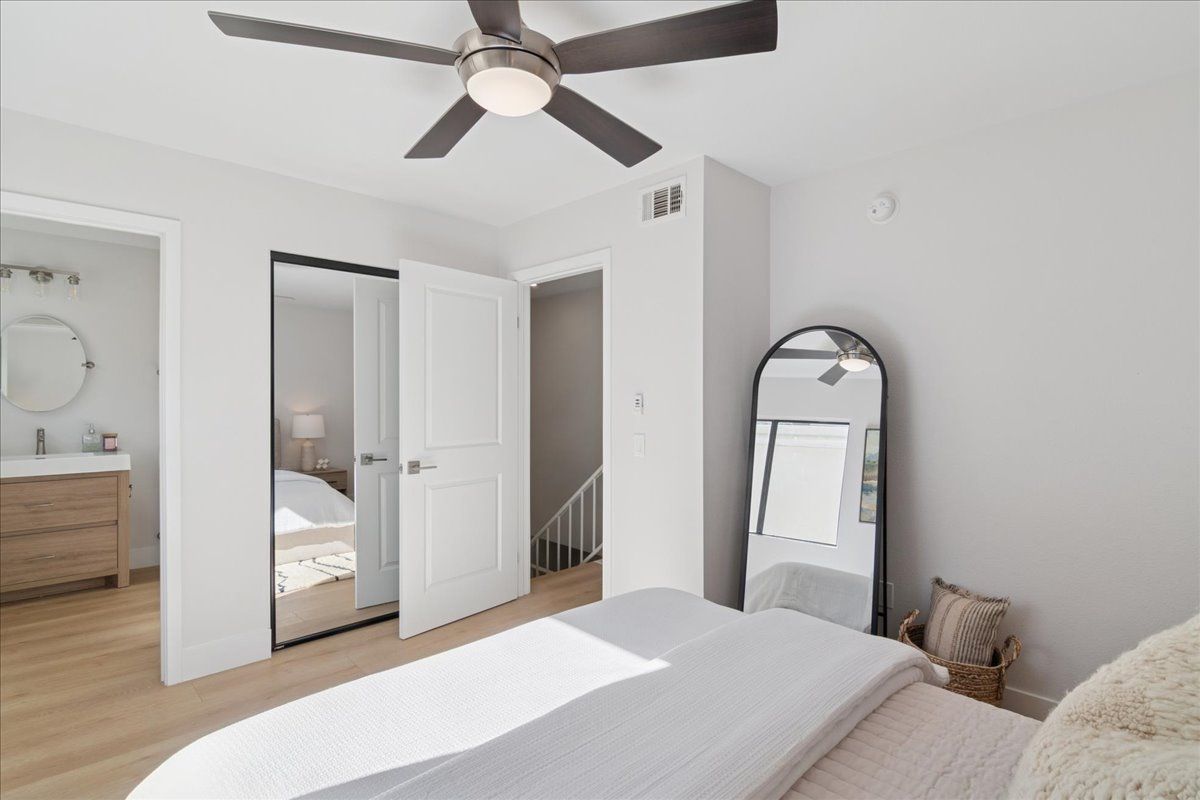 Bright bedroom with ceiling fan, mirrored closet doors, and standing mirror on hardwood floor