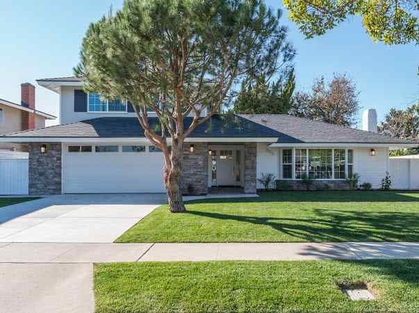Two-story house with white walls, gray roof, and a large tree in the front yard.