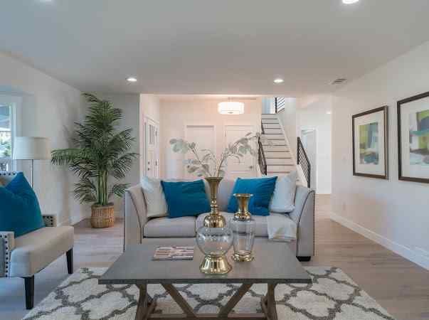 Living room with neutral tones, teal pillows, coffee table, and a staircase in the background.