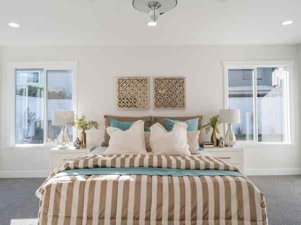 Bedroom with striped comforter, windows, nightstands, and decorative wall art.