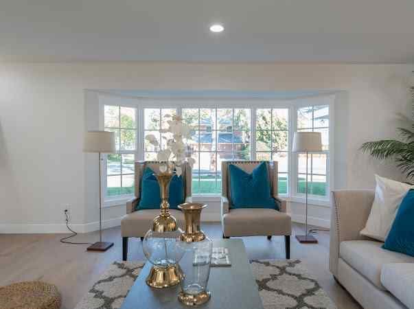 Living room with beige furniture, teal pillows, and large bay window.