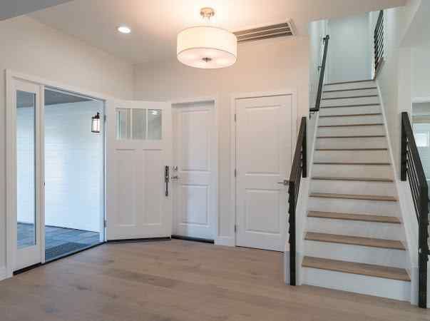 Entryway with stairs, white doors, and light fixture; hardwood floors and black metal railing.