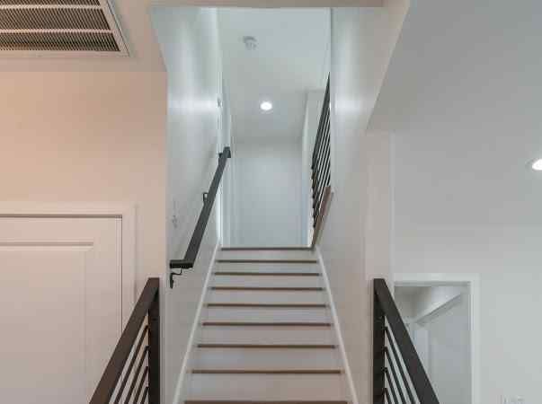 Staircase in a white room with brown handrails and stairs leading to a light at the top.