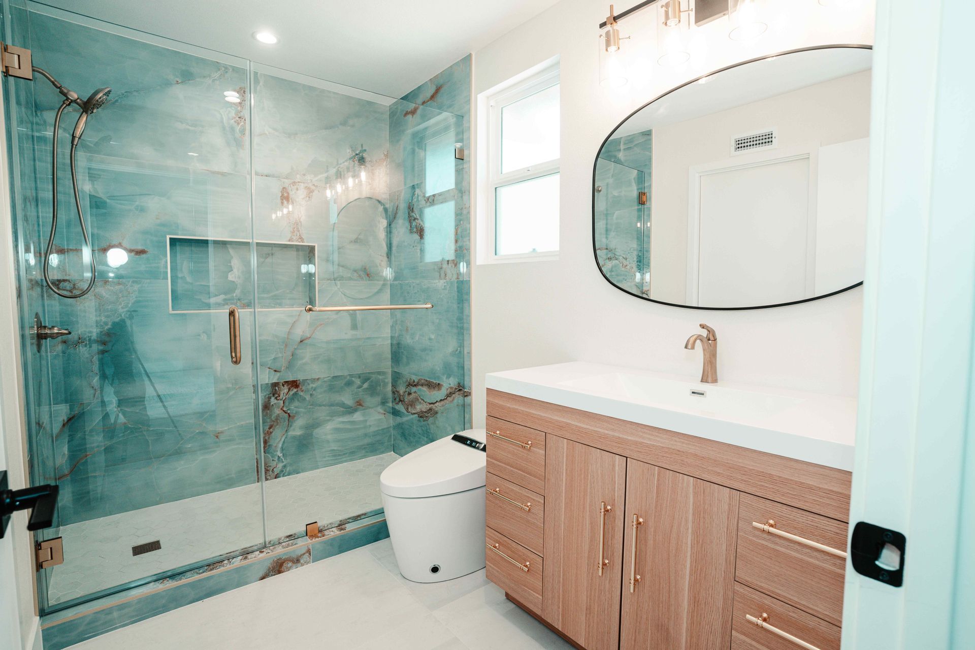 Modern bathroom with teal glass shower, white toilet, and wood vanity with round mirror
