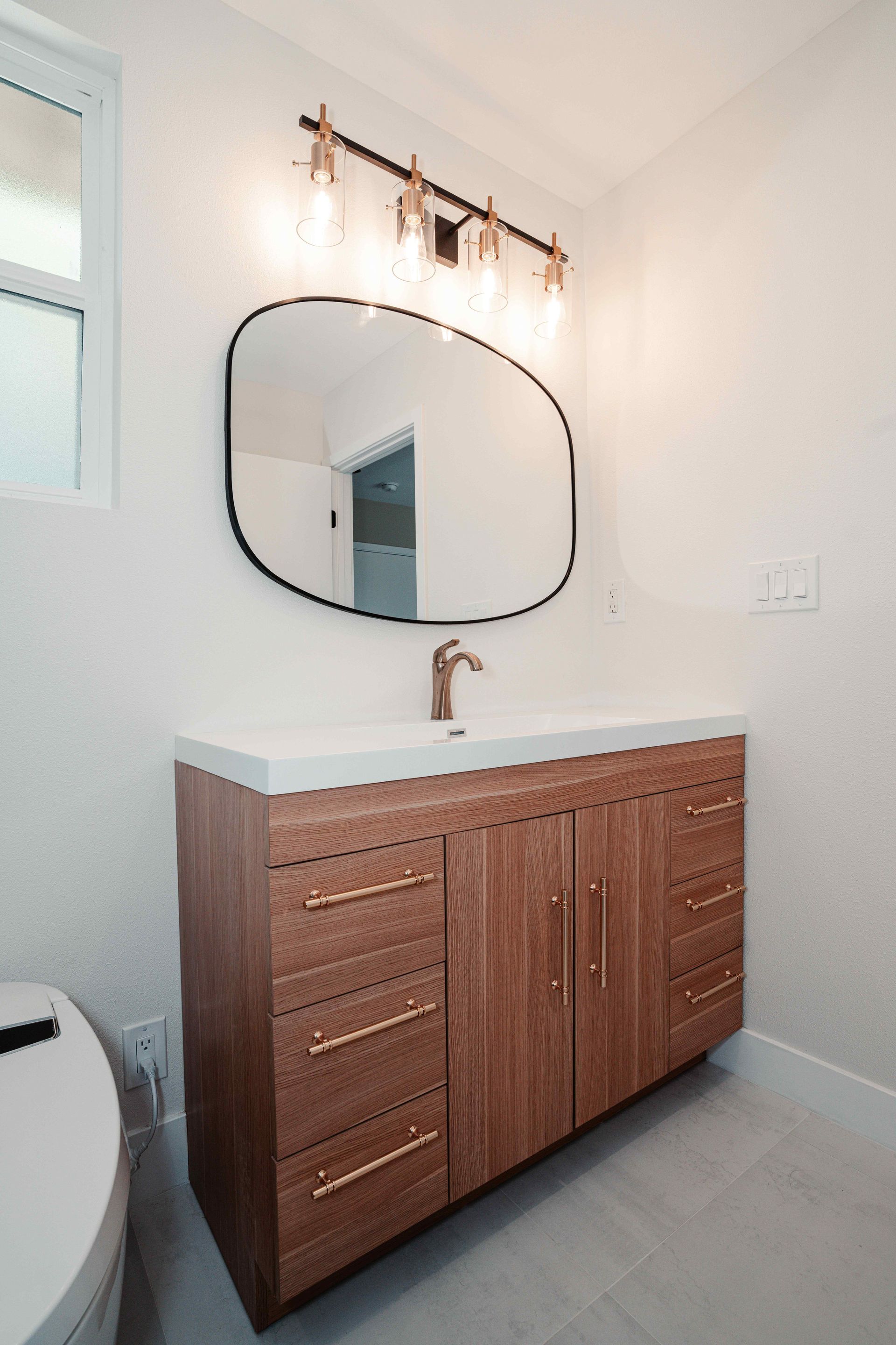 Modern bathroom vanity with wood cabinets, white countertop, oval mirror, and wall light fixture