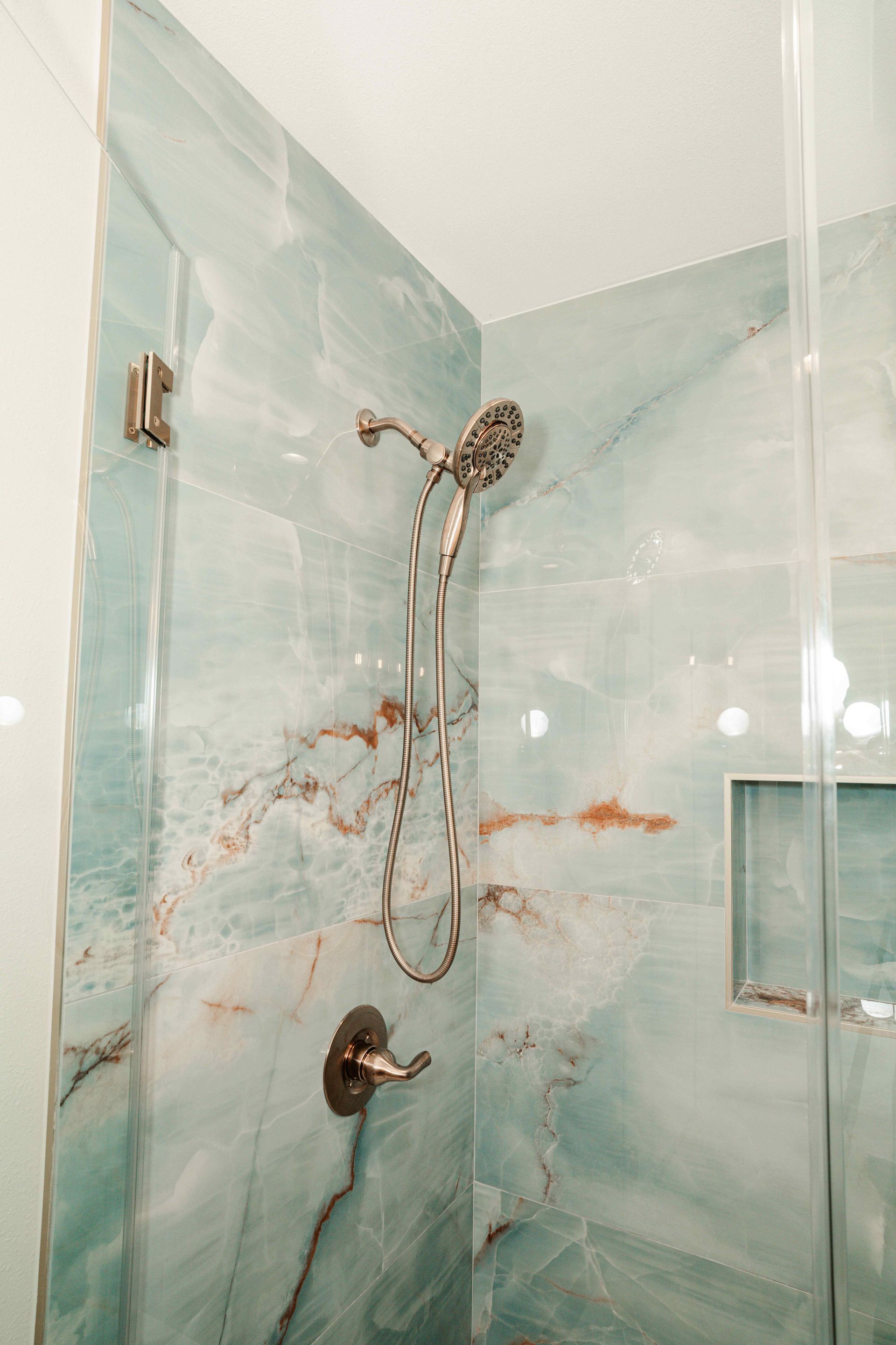 Glass shower stall with teal marble-look tile and chrome fixtures