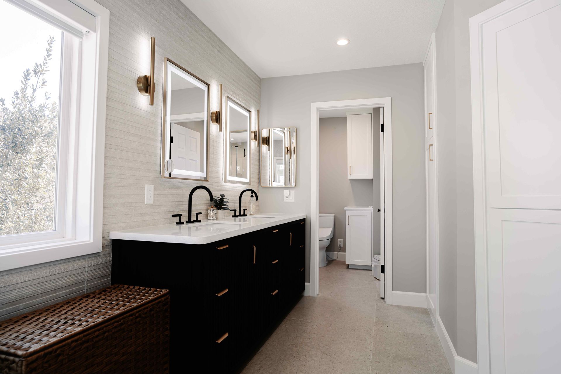 Bright bathroom vanity with double sinks, black cabinets, mirrors, and a large window.