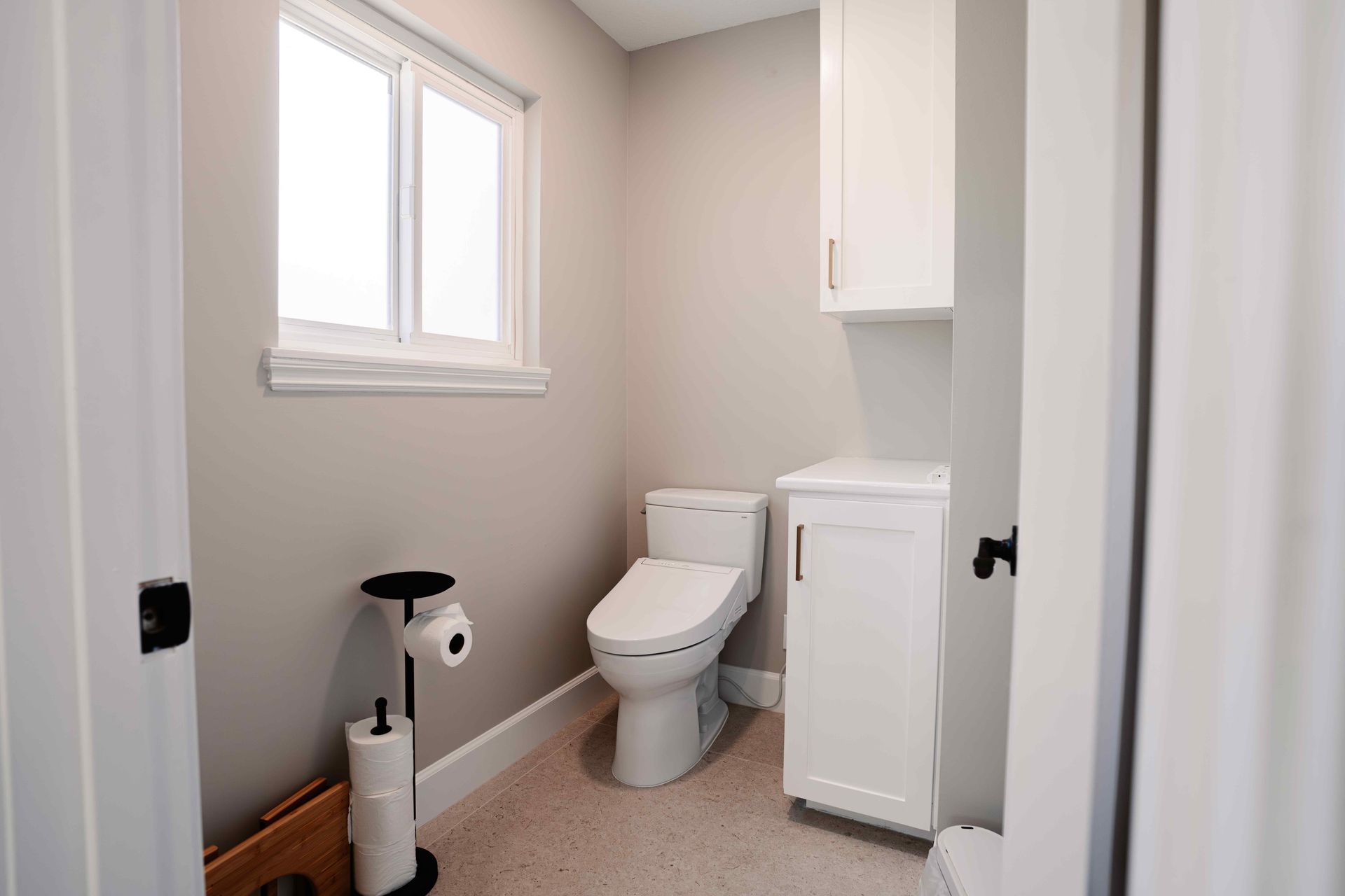 Small bathroom with toilet, white cabinet, window, and a black-and-white floor cleaner near the sink area.