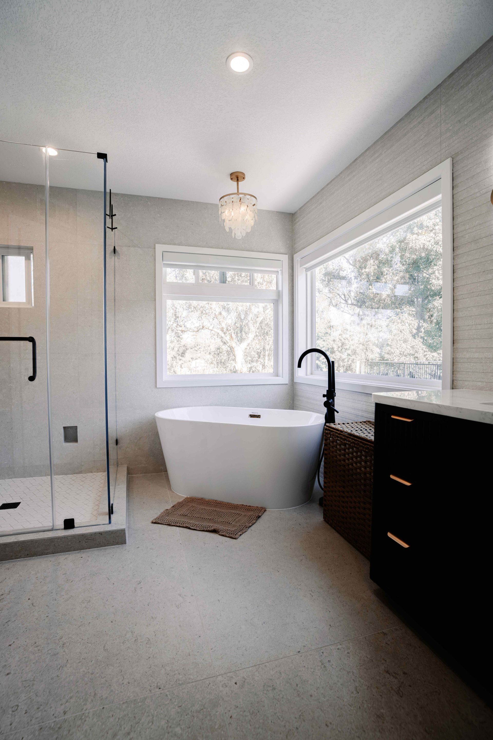 Bright modern bathroom with freestanding tub, glass shower, and double windows.