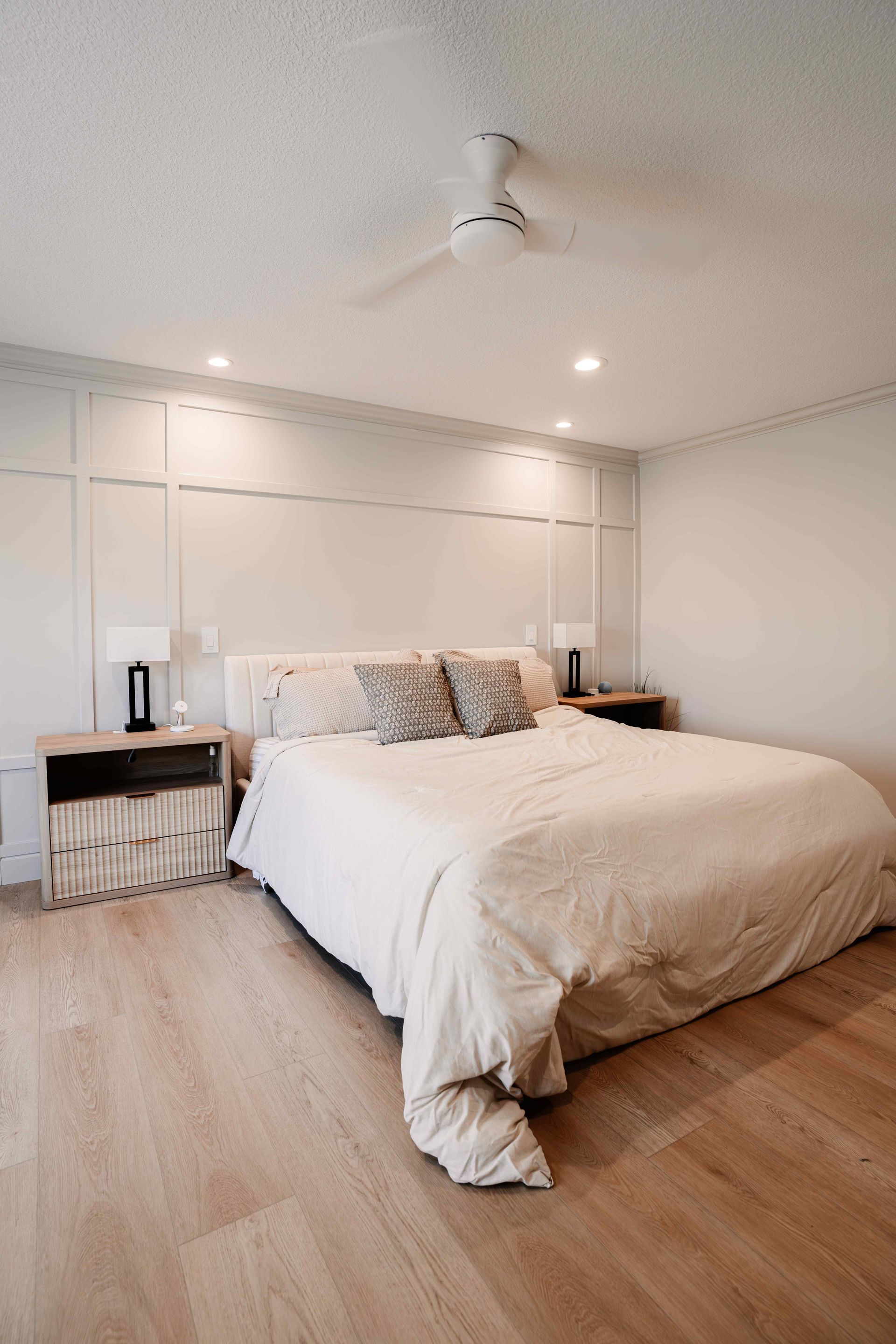 Bright minimalist bedroom with a white bed, wood floor, nightstands, and recessed ceiling lights