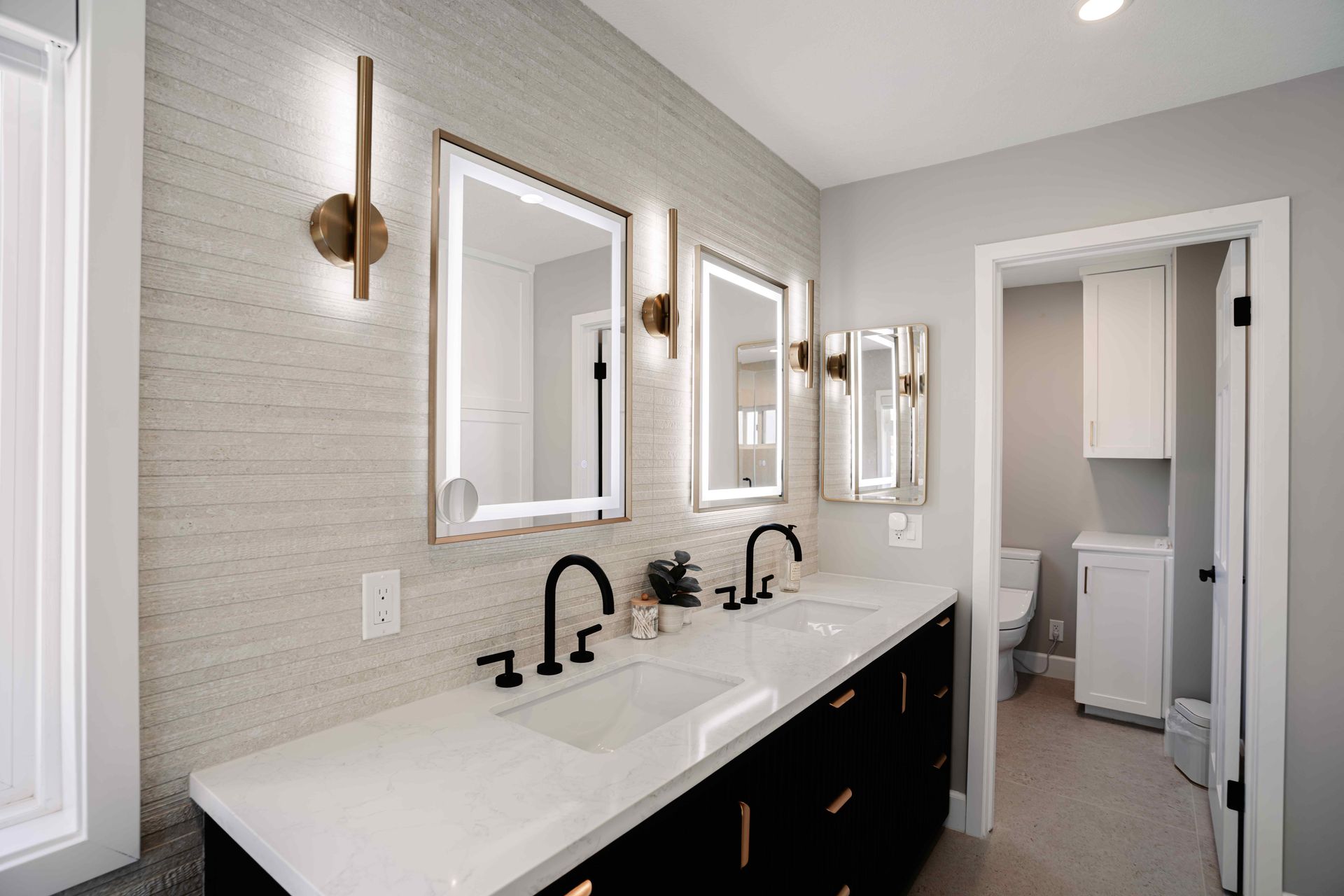 Bright modern bathroom with double vanity, black fixtures, and mirrors beside an open doorway