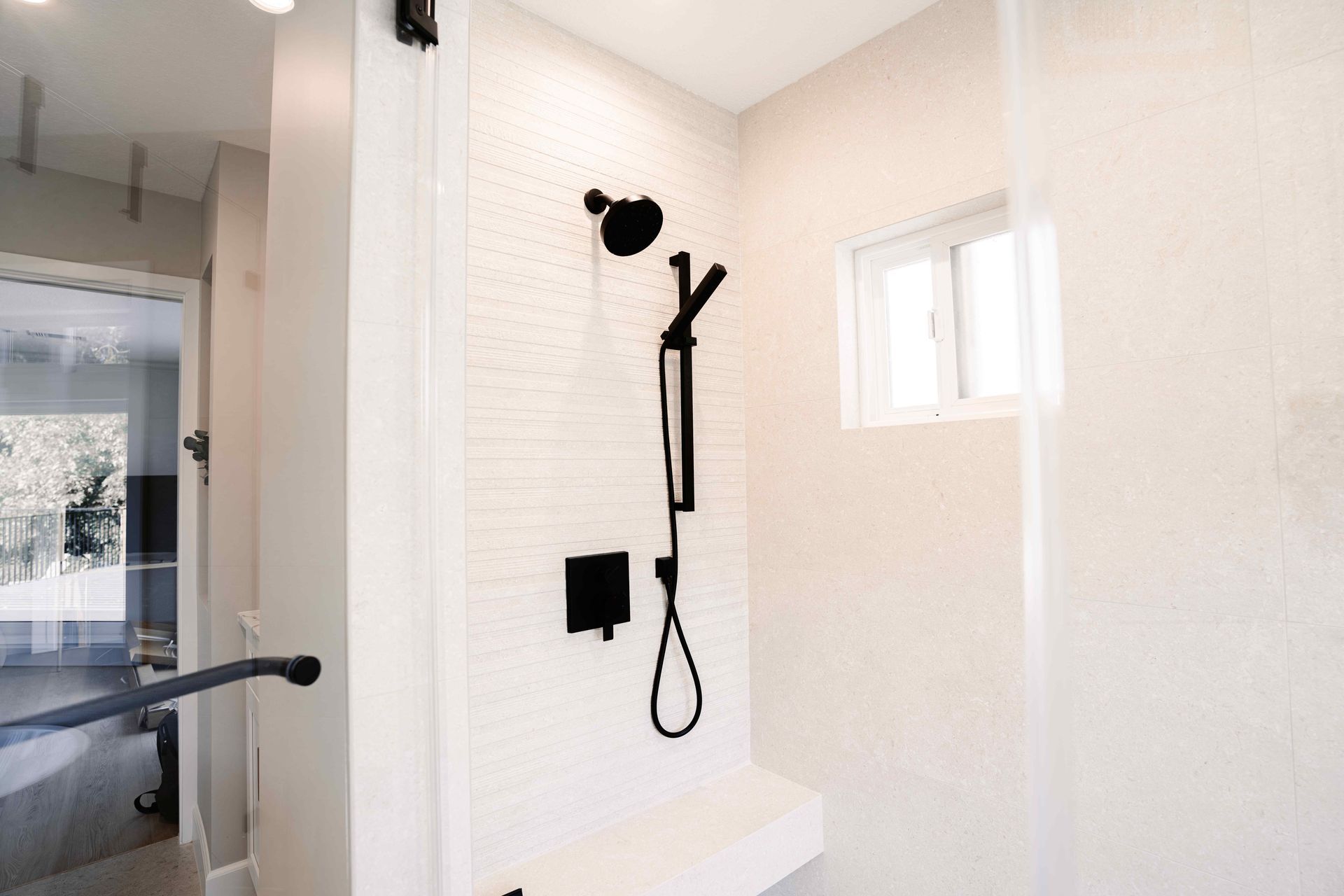 Modern shower interior with wall-mounted handheld showerhead, black fixtures, and a small window.