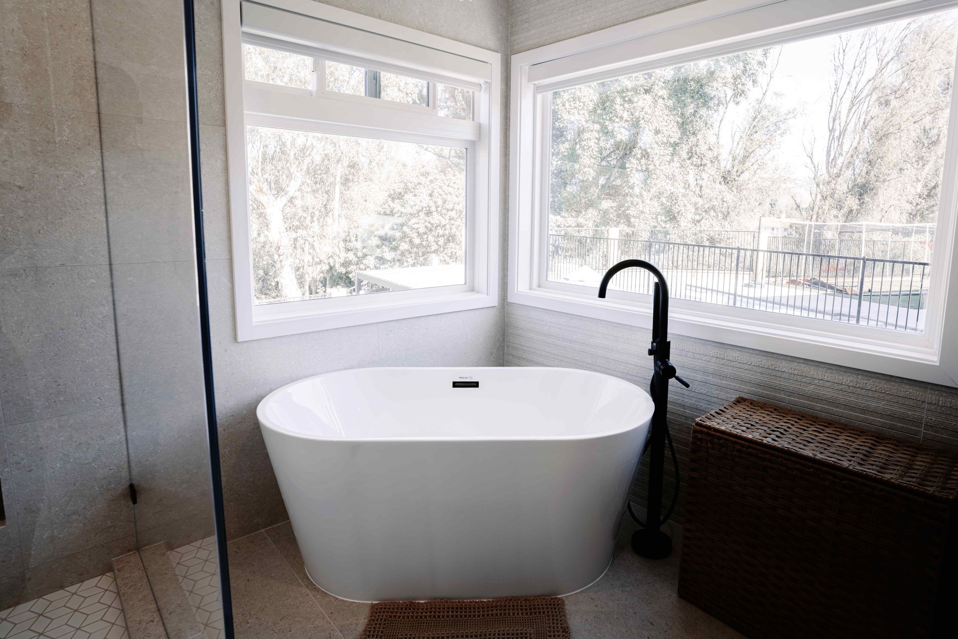 Bright bathroom with a white freestanding tub, black faucet, and large windows overlooking trees.