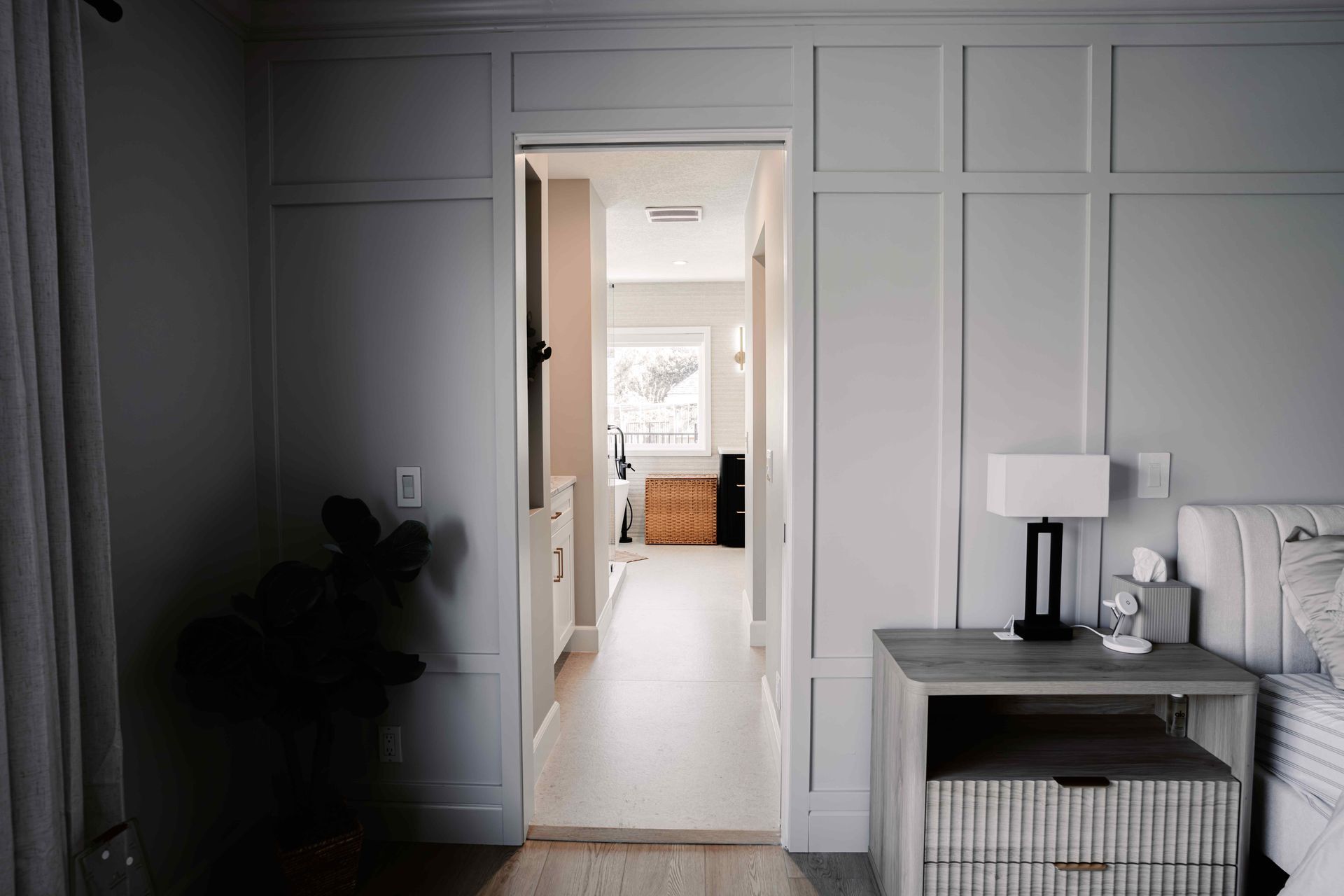 Modern gray-paneled hallway with an open doorway to a bright room and a small side table with lamp and decor