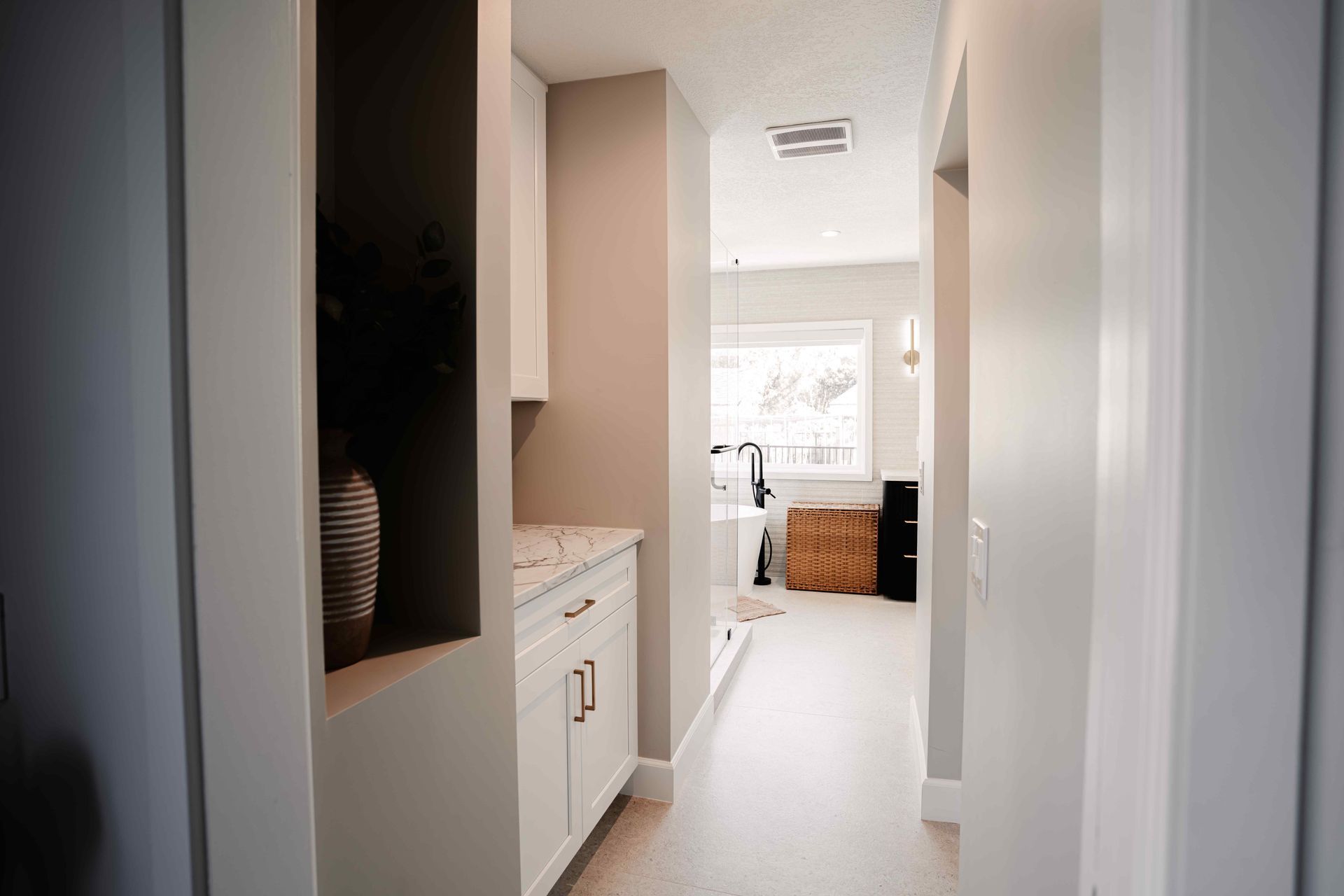 Narrow hallway with built-in cabinets leading to a bright room with a window and wicker storage bench.