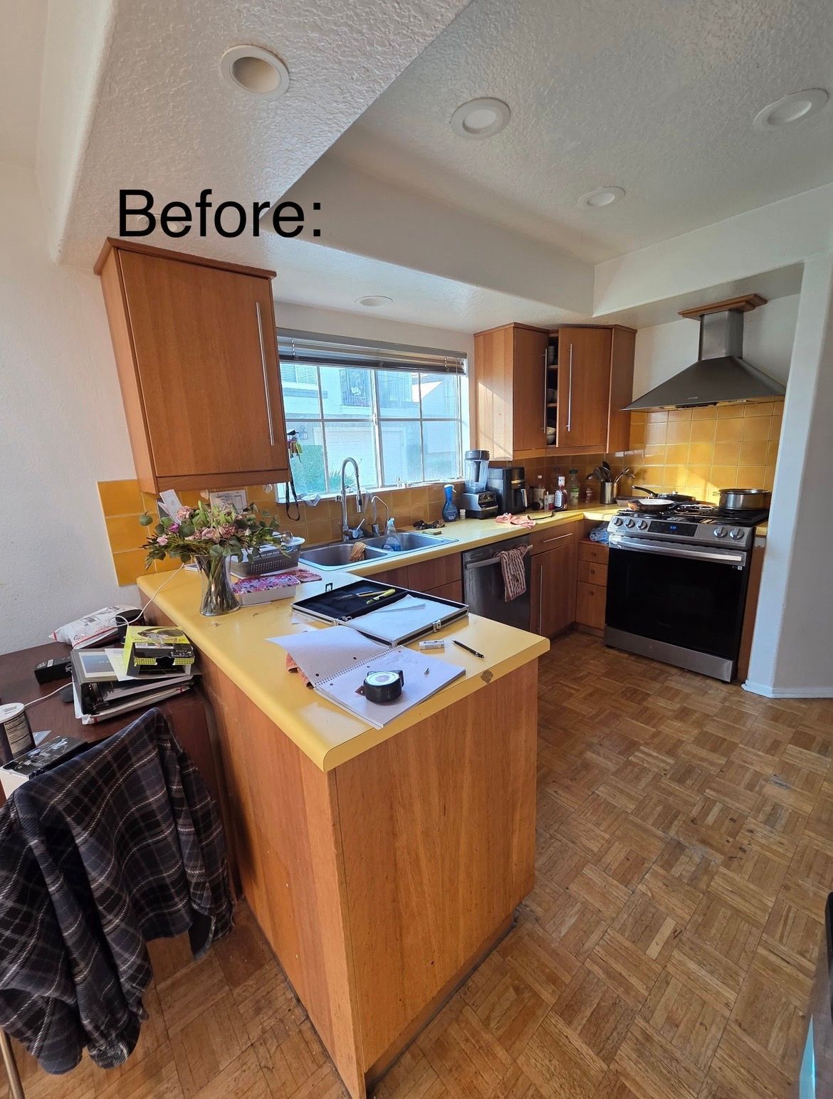 Before: cluttered kitchen with wood cabinets, island, window, and stove under warm lighting