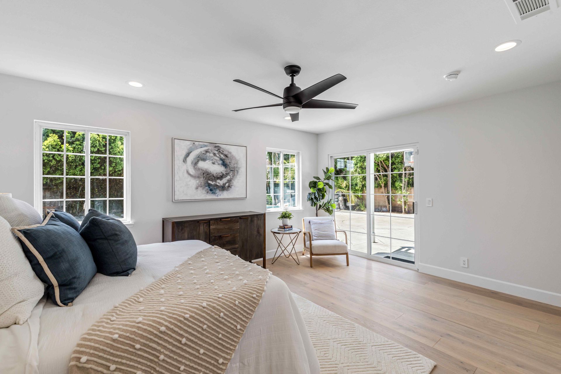 Bright bedroom with a bed, dark dresser, ceiling fan, and sliding glass doors to a patio.