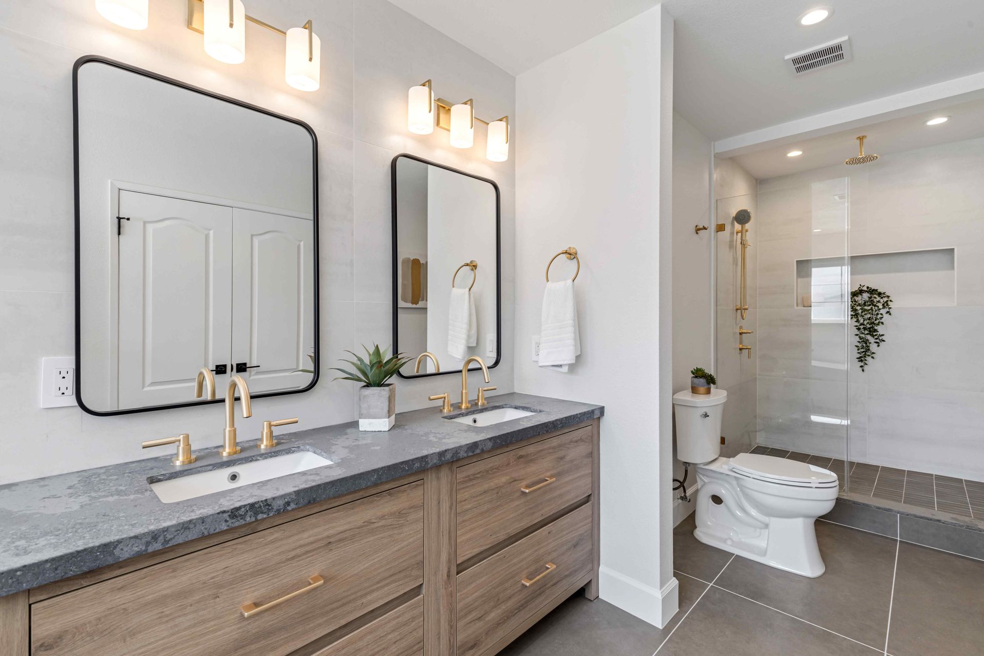 Modern bathroom with double vanity, gold fixtures, large mirror, and separate toilet area