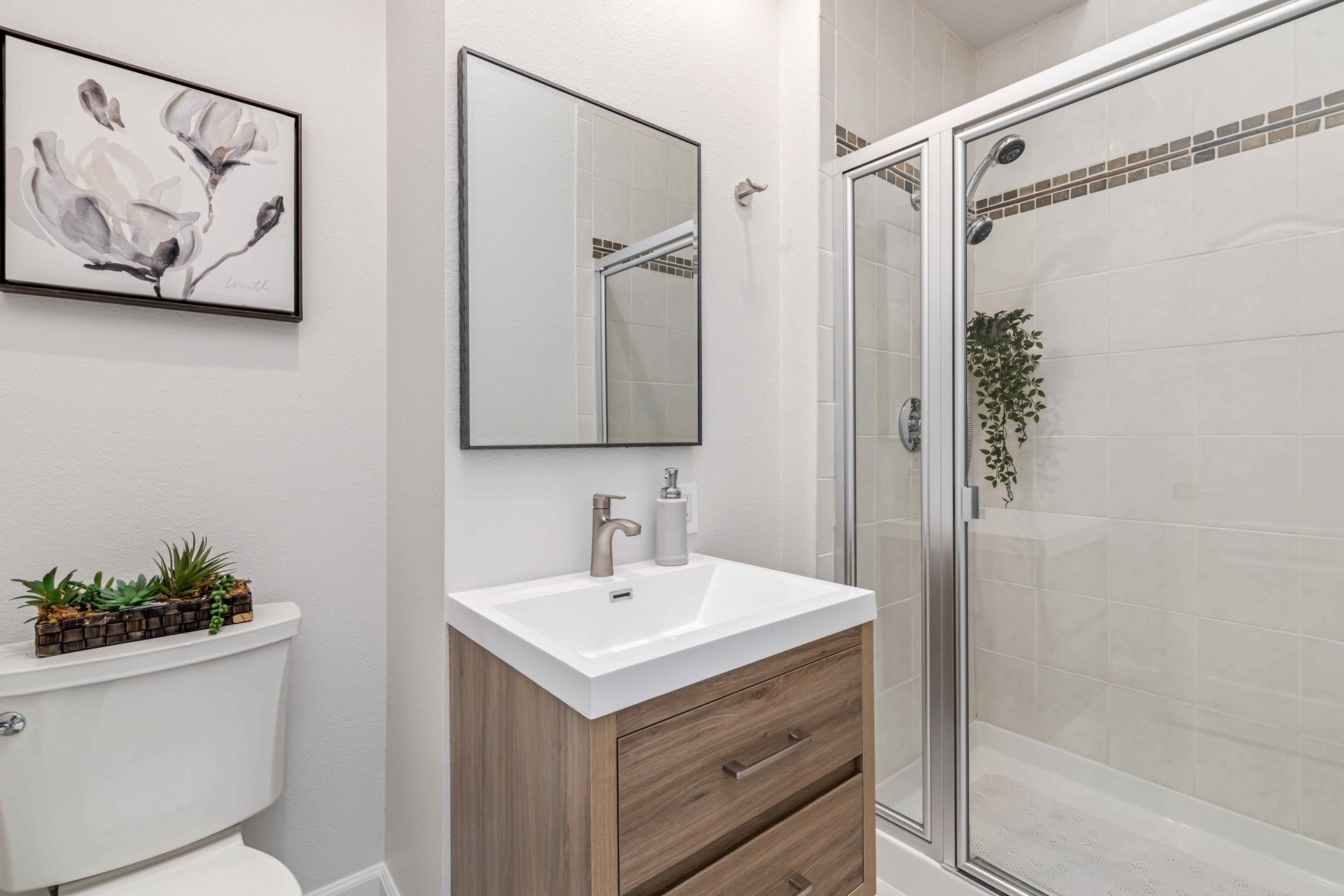 Bright bathroom with sink vanity, mirror, wall art, and glass shower door