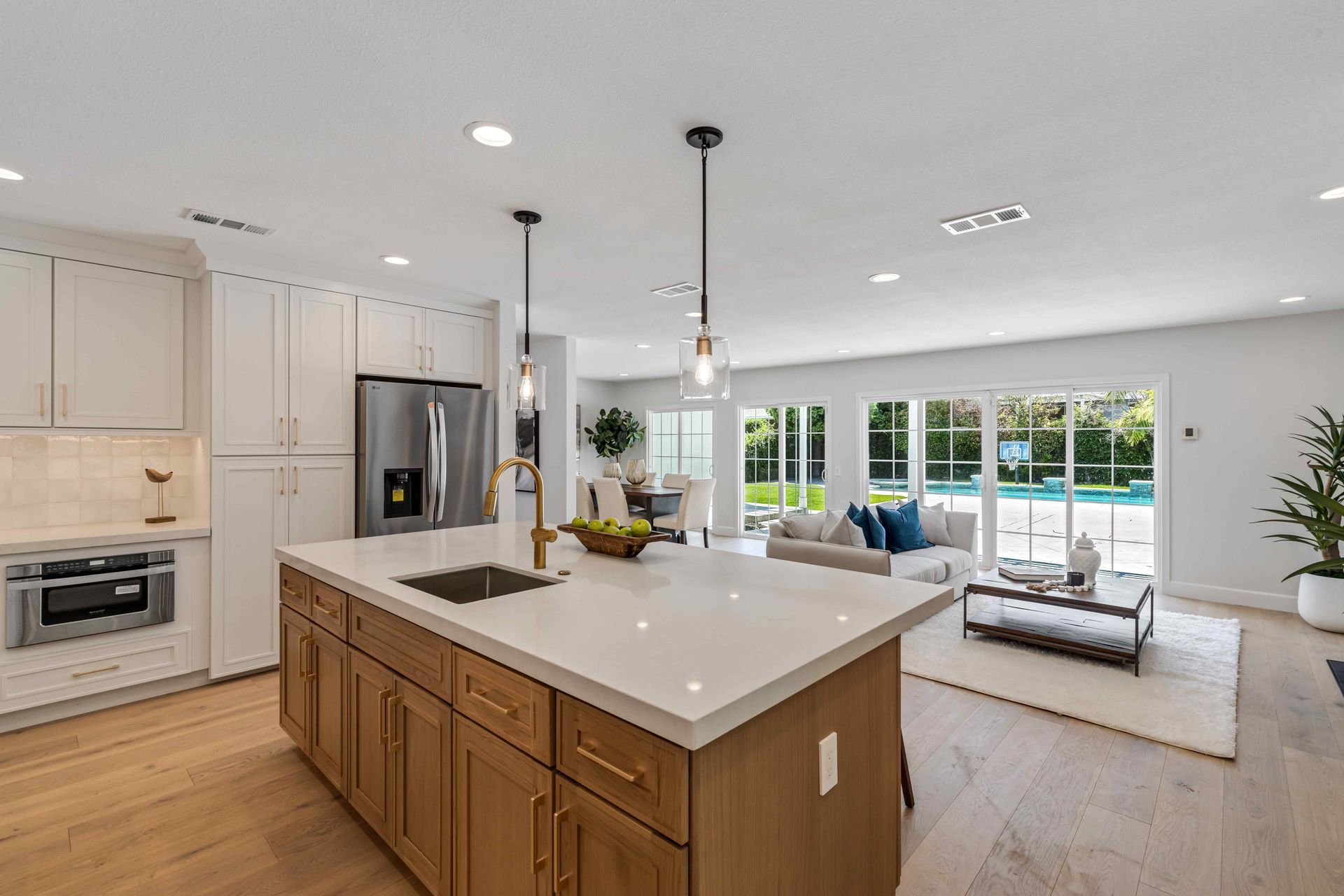 Open-concept kitchen and living room with island, white cabinets, and large sliding glass doors