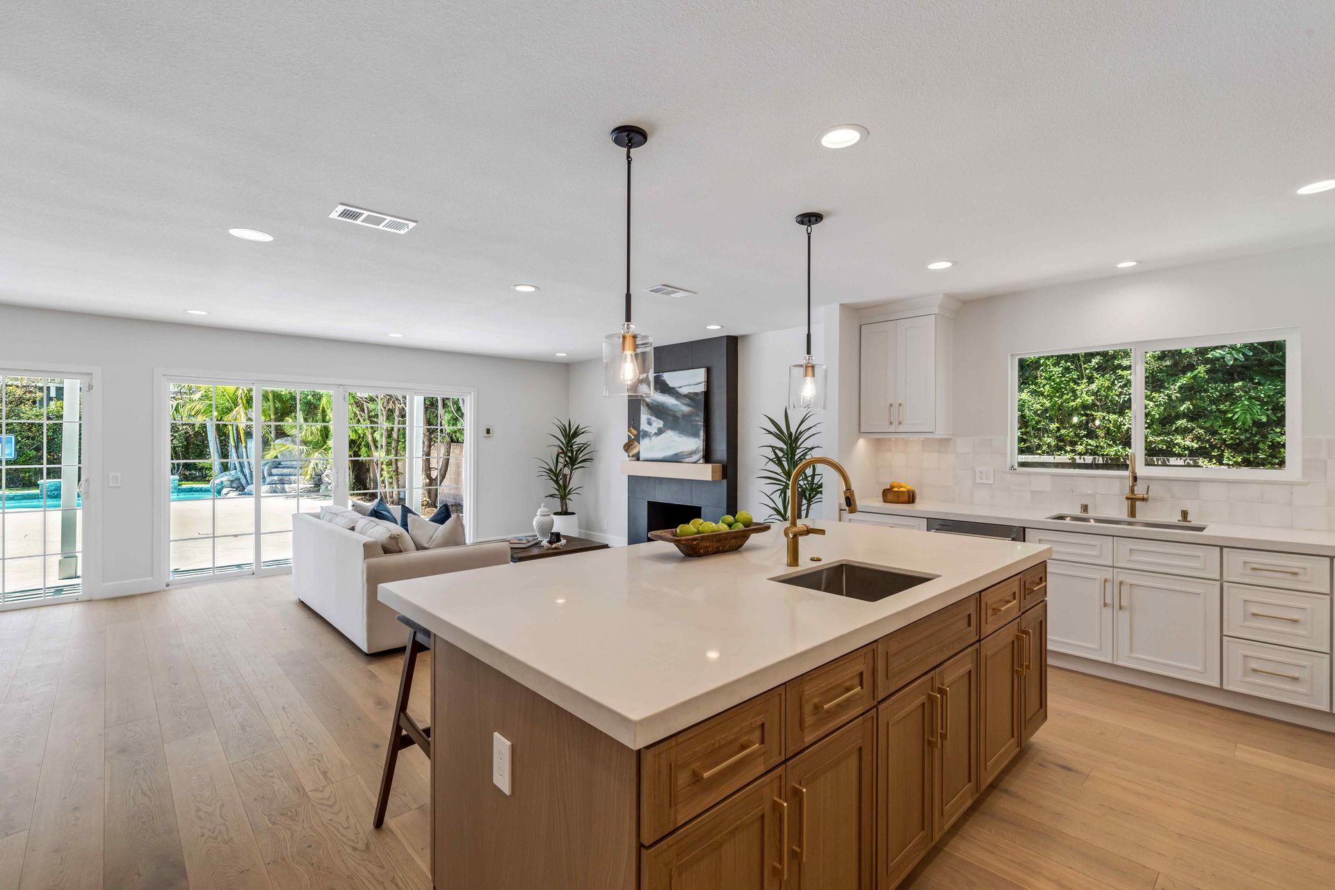 Bright modern kitchen with a large island, white cabinets, wood floors, and open view to a living area
