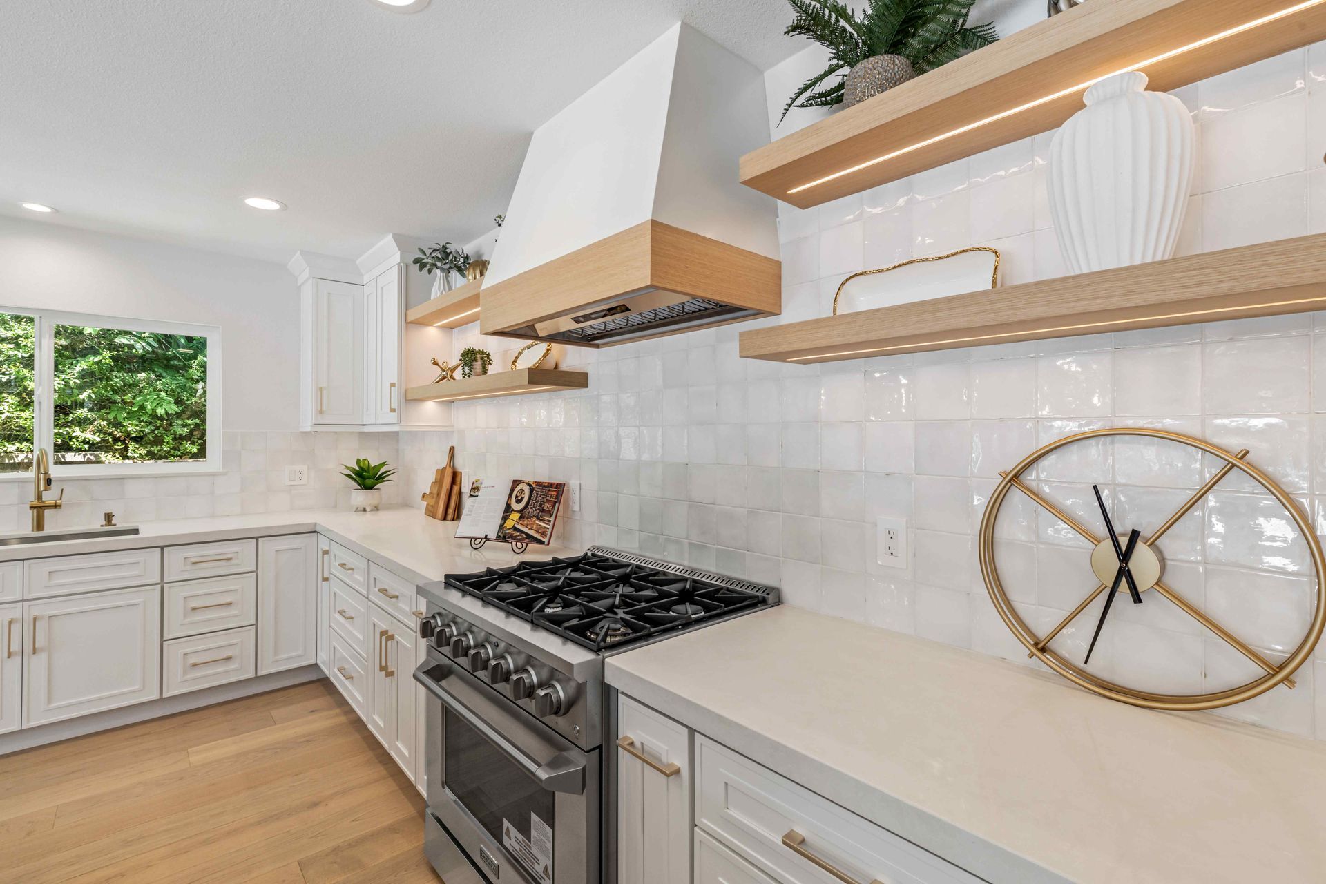 Bright white modern kitchen with wood shelves, stainless stove, and light countertops.