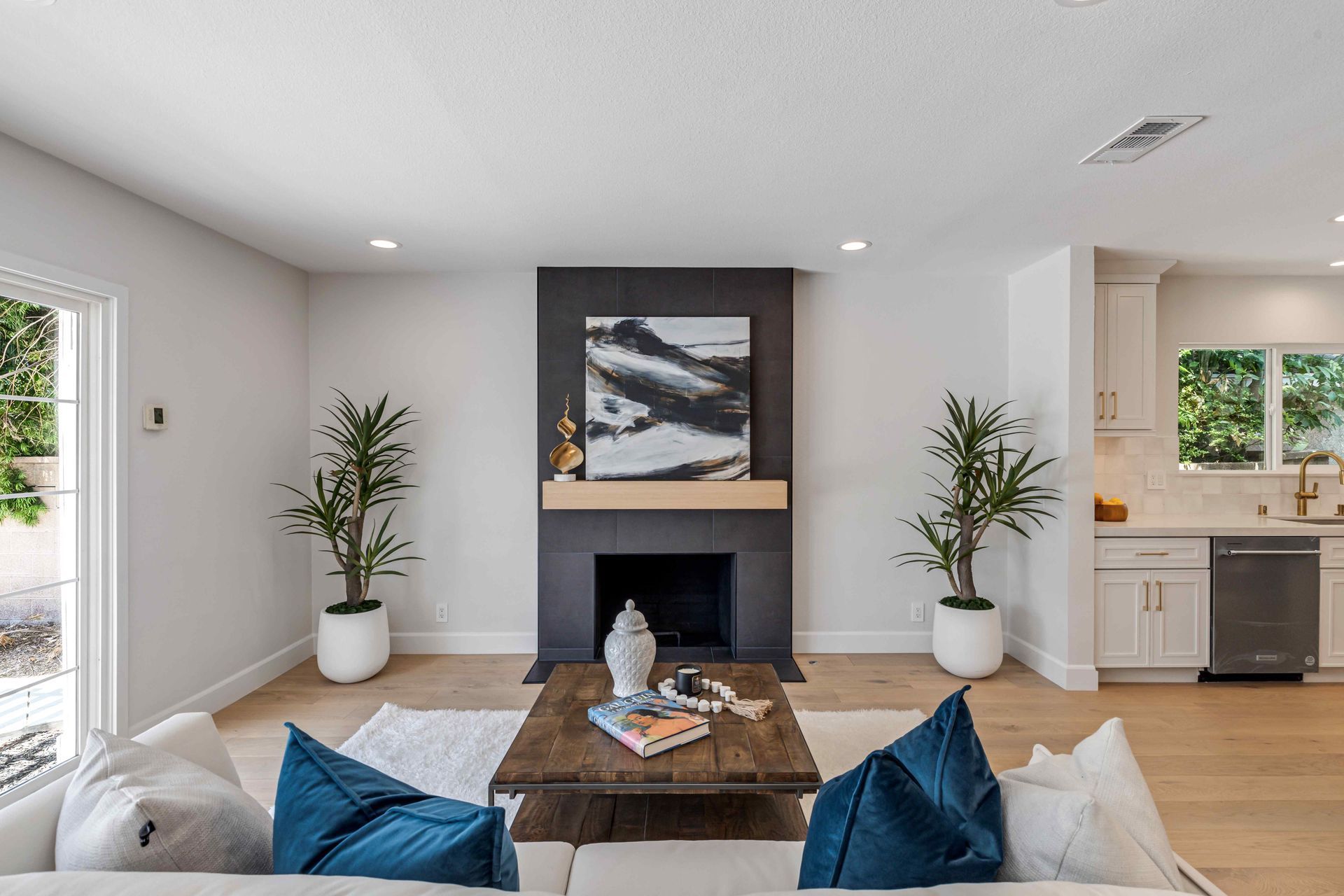 Modern living room with fireplace, framed art, blue pillows, and potted plants.