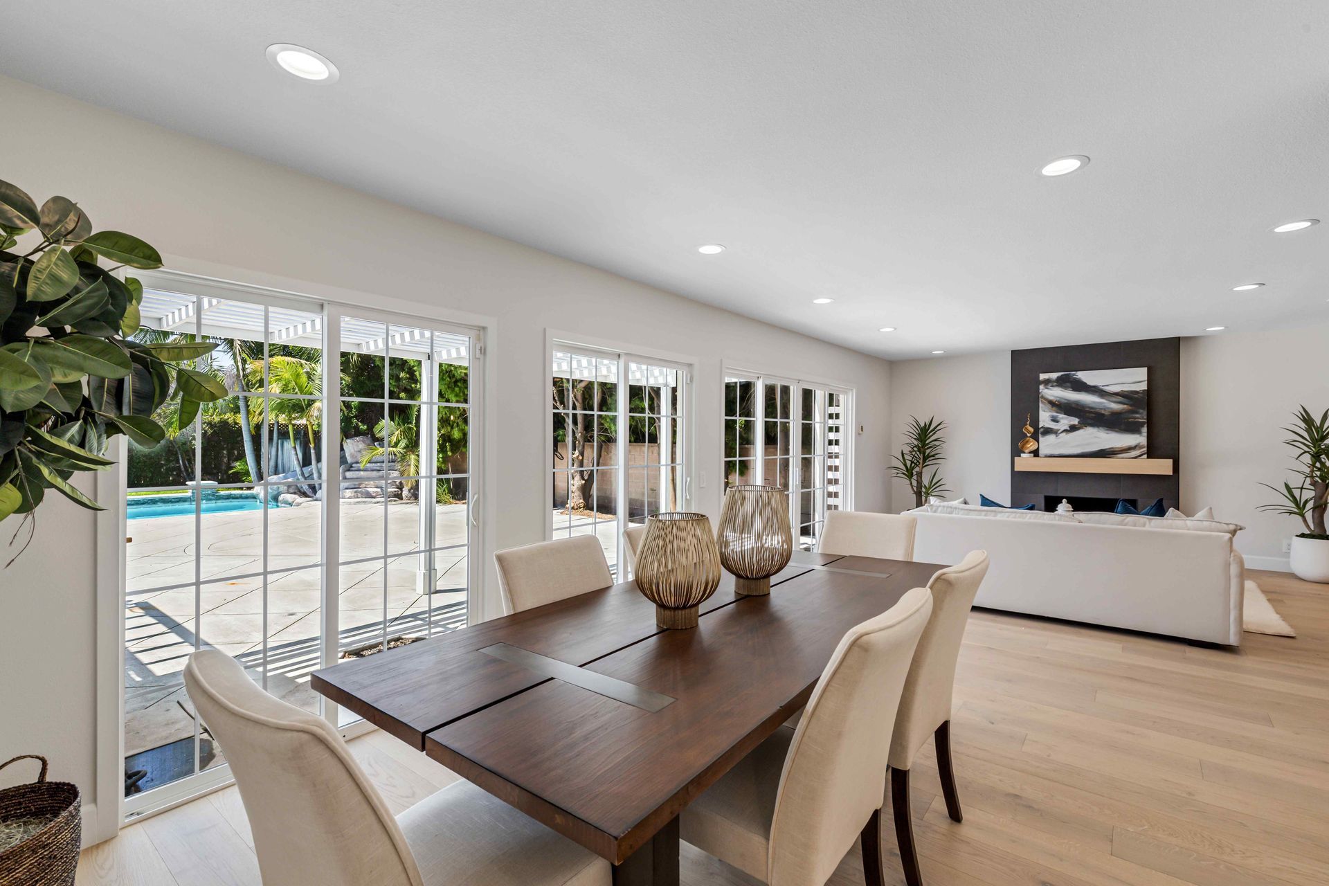 Bright dining room with long table, cream chairs, and French doors opening to a backyard pool