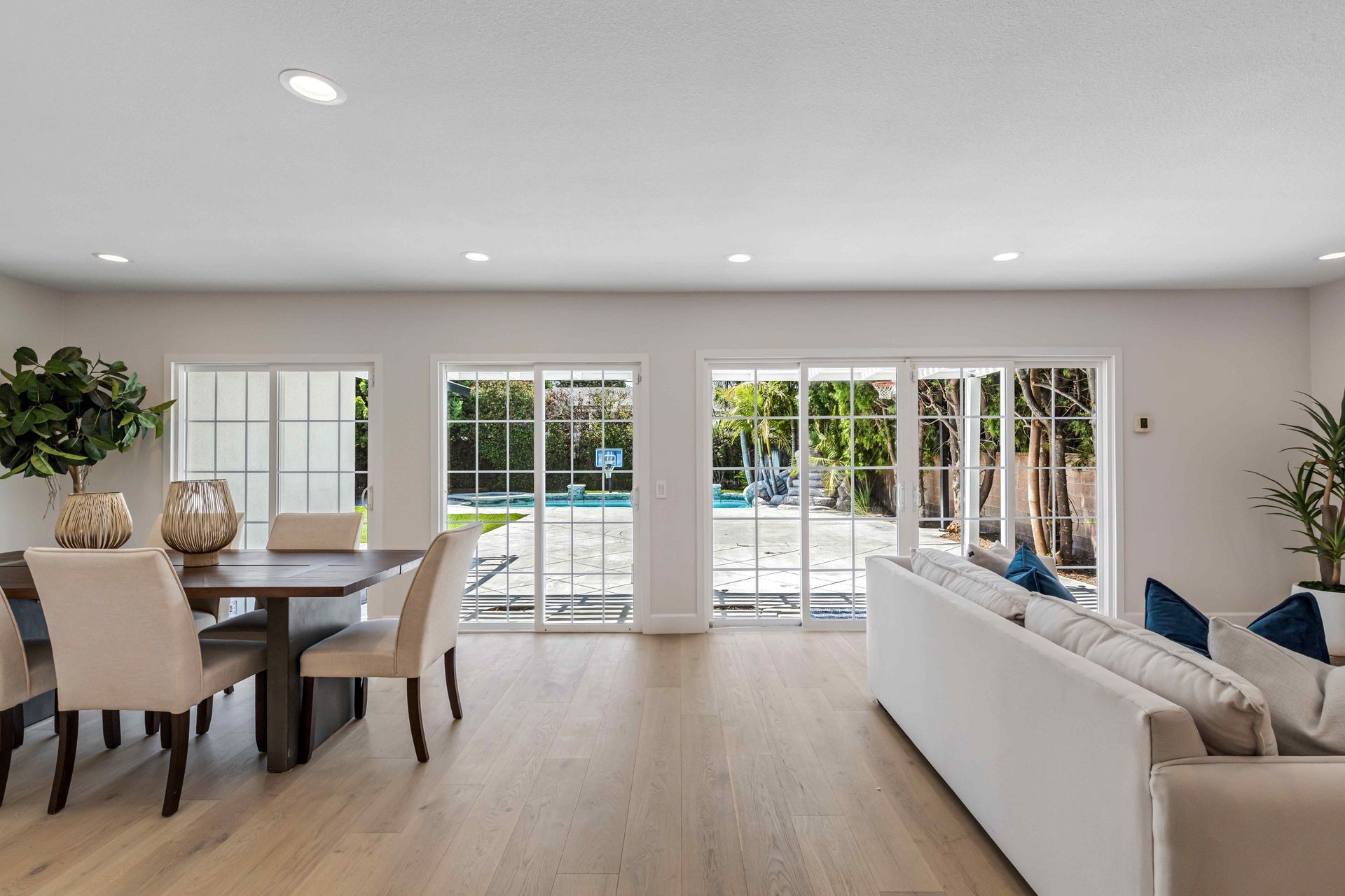 Bright open living and dining room with white walls, wood floors, dining table, sofa, and glass doors to a patio