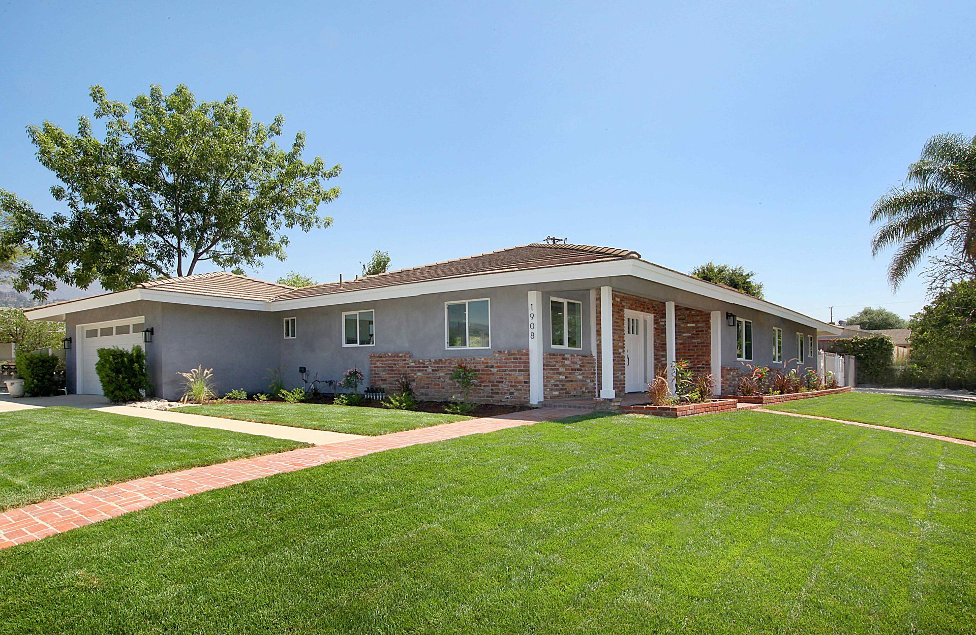 A light gray single-story house with a brick walkway and a large green lawn.