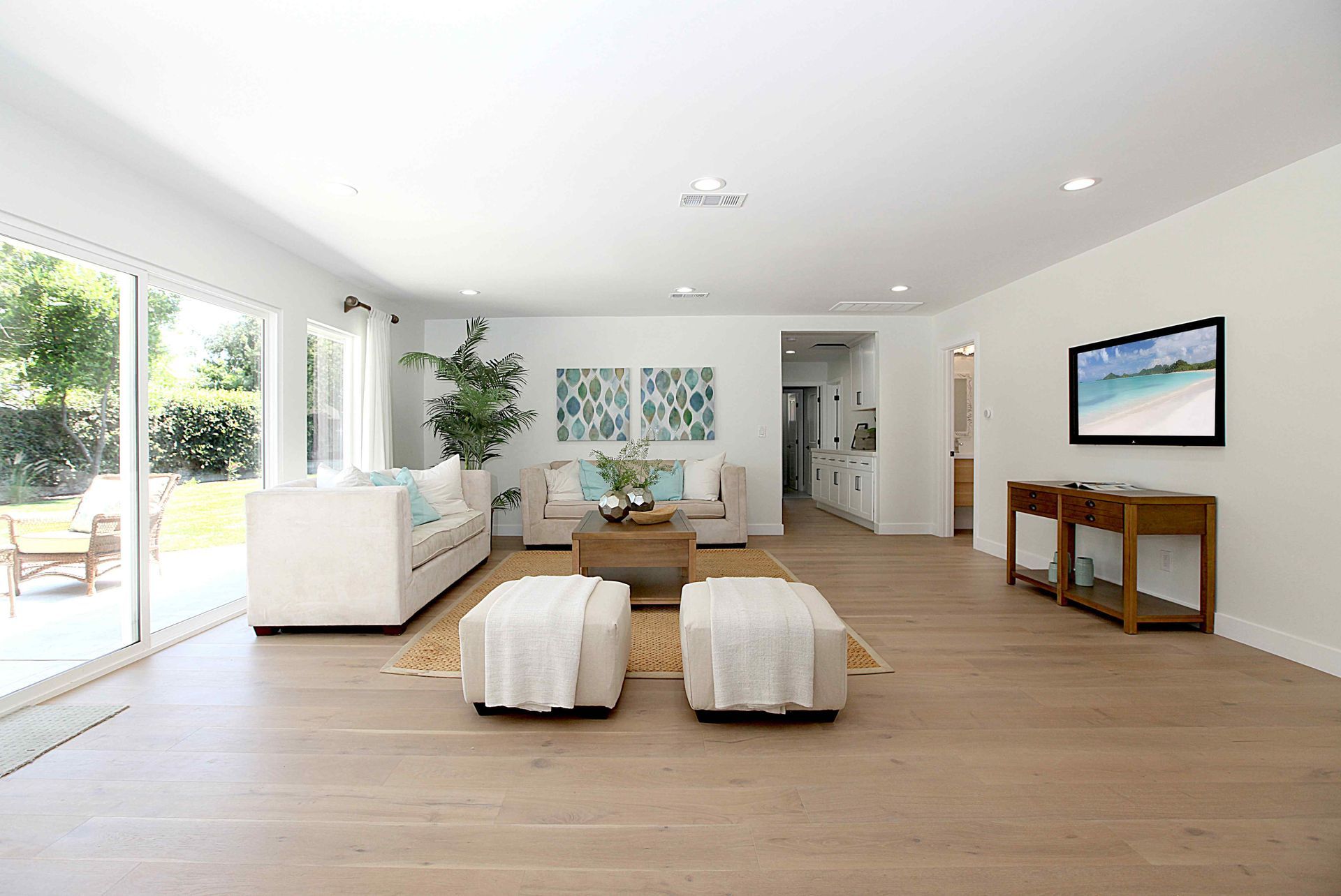 Bright, open living room with white walls, light wood floors, sliding glass doors to a backyard, and a TV.