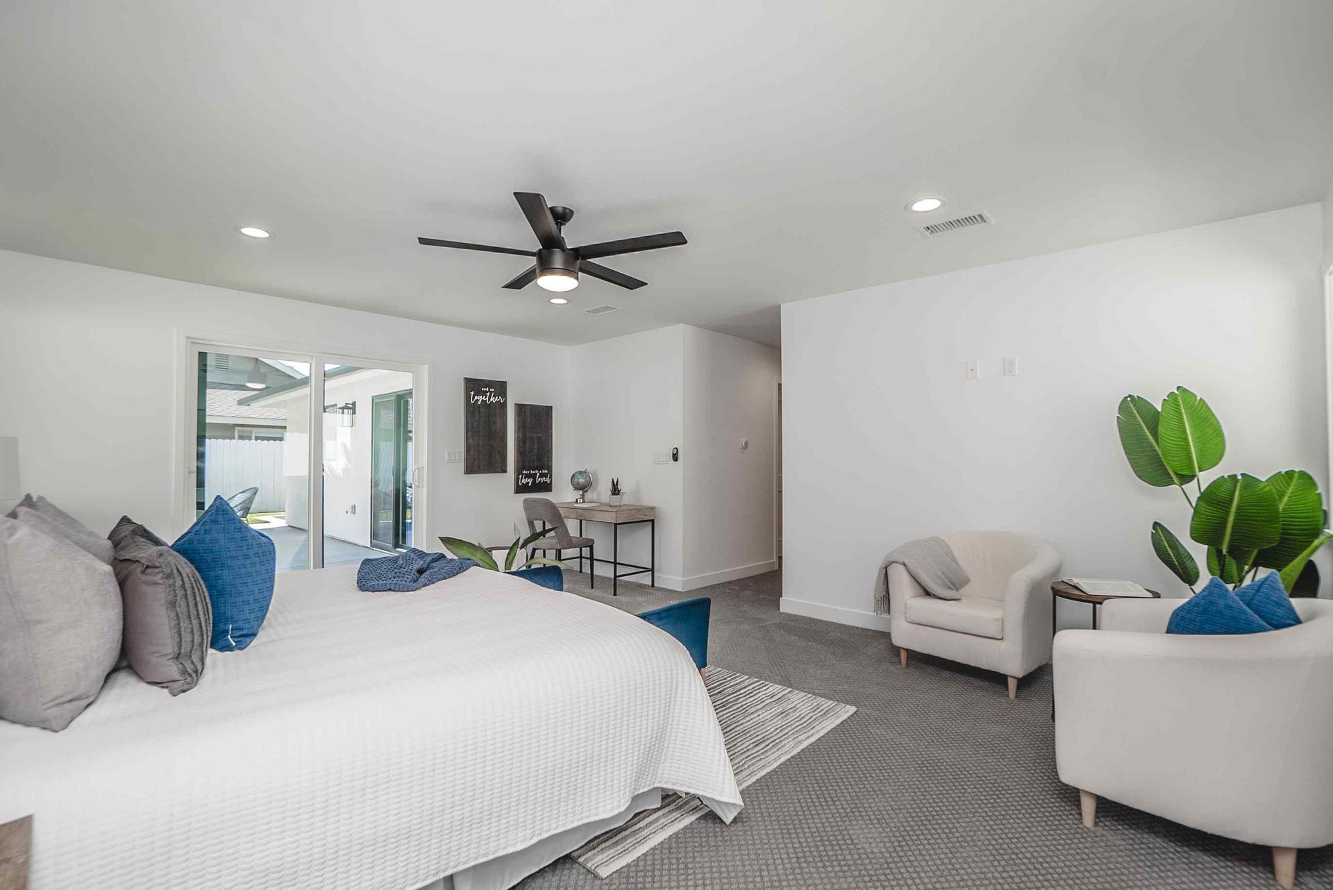 Spacious bedroom with white walls, king bed, seating area, and desk. Sliding glass doors lead to the outdoors.
