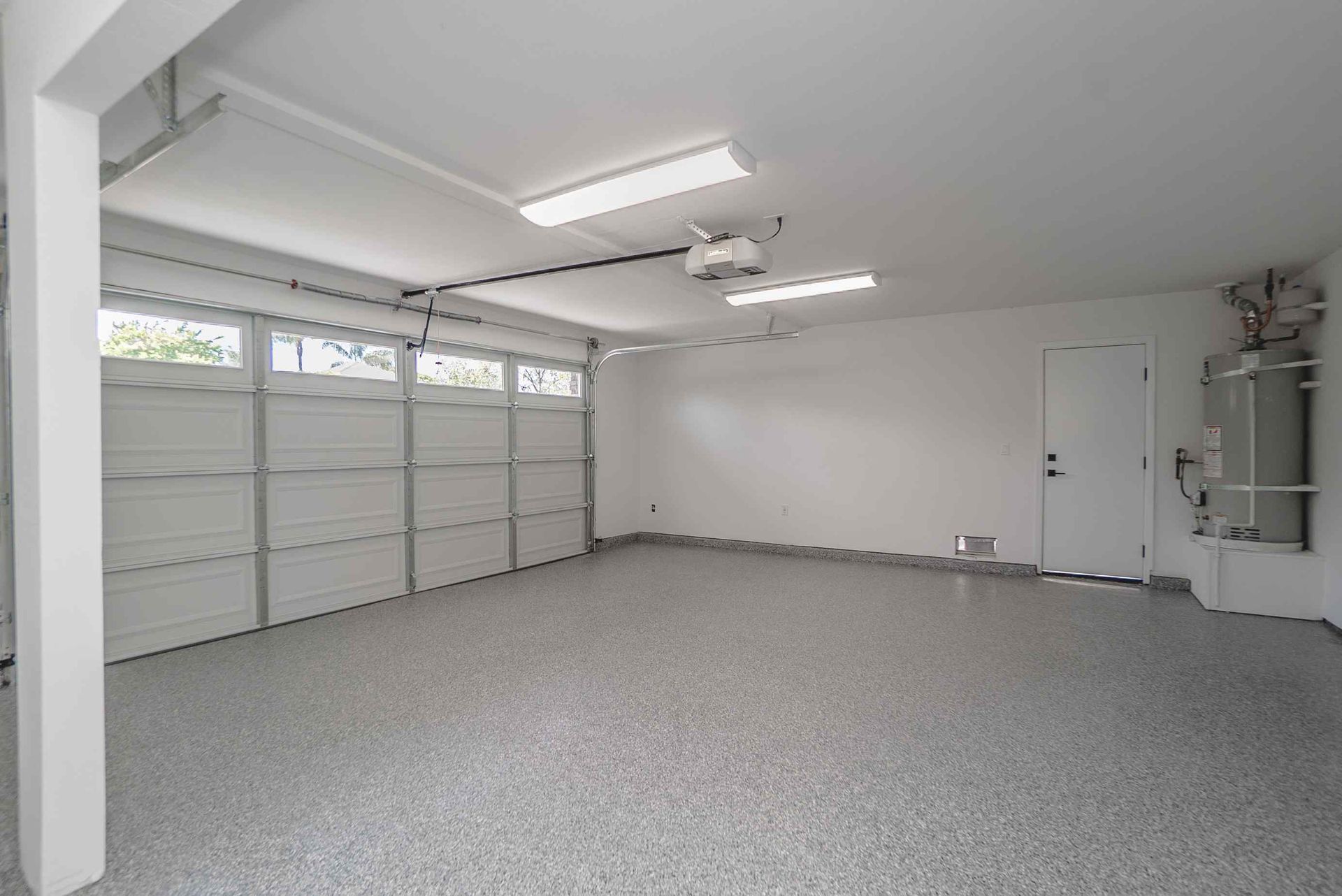 Empty, well-lit garage with a white door, speckled gray floor, and a closed garage door.
